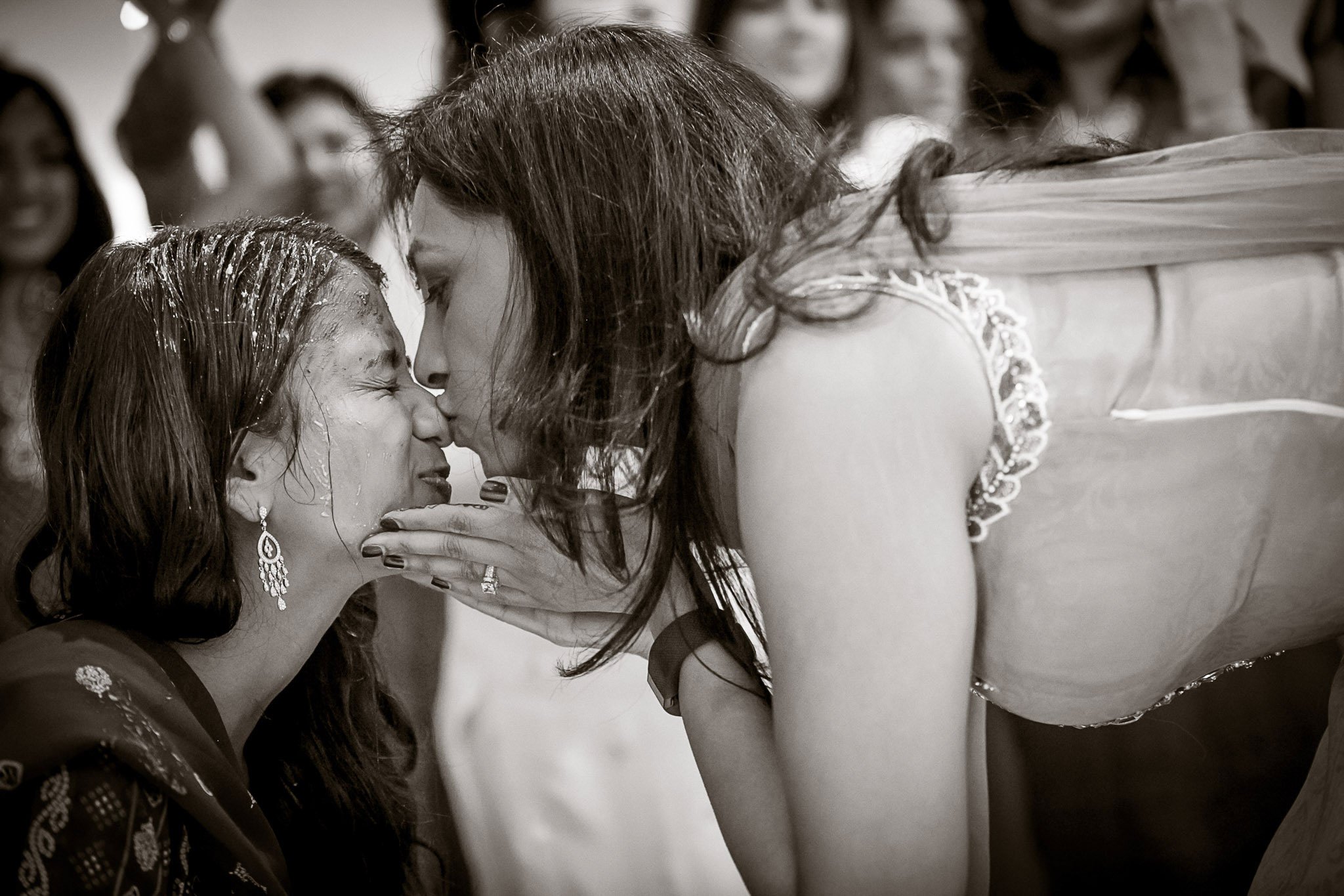 A woman gently touching another woman's face during a close, intimate moment at what appears to be a celebration or ceremony.