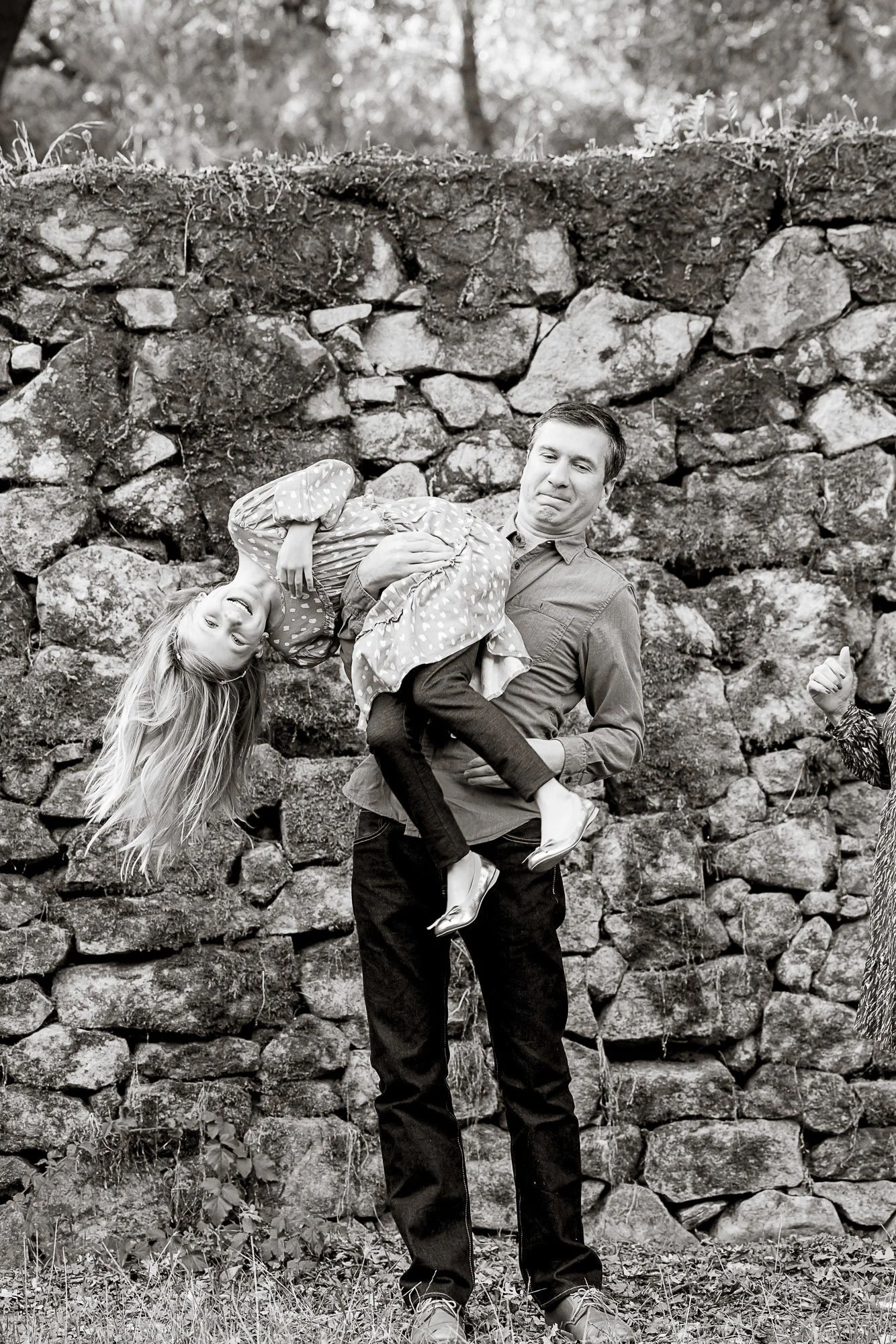 A man holding a young girl in a polka dot dress in front of a stone wall
