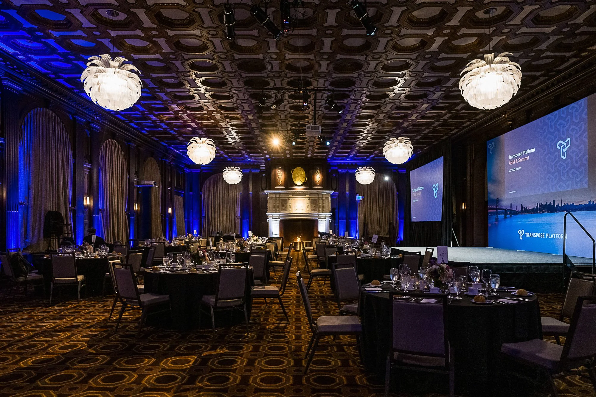 Elegantly decorated Julia Morgan Ballroom, large white chandeliers hanging from a decorative ceiling, draped curtains, and a large stage with screens displaying the 'Transposrt Platform' logo and cityscape background.