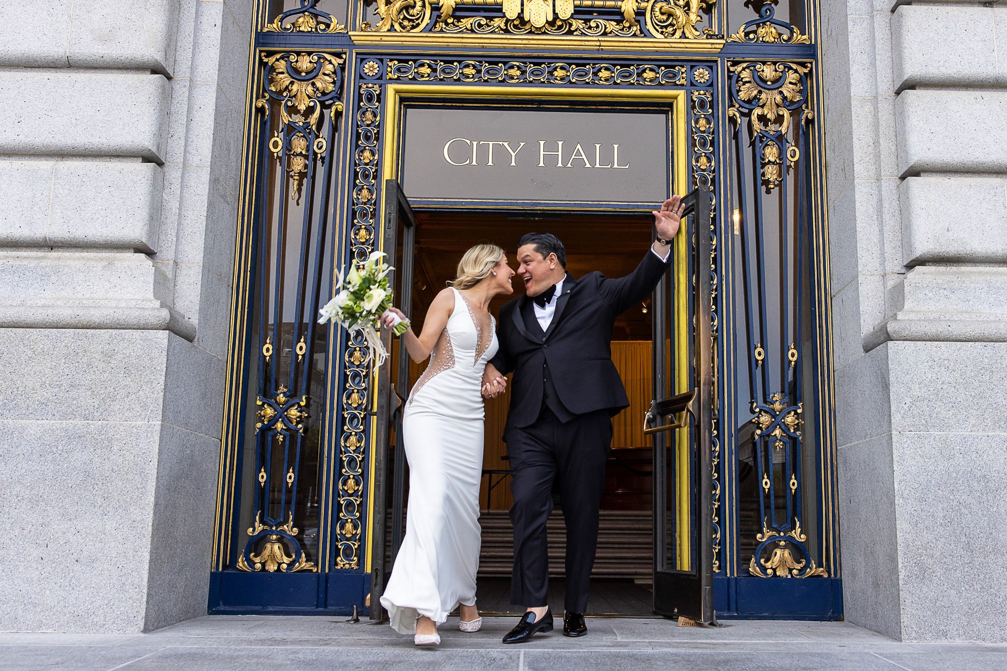 Bride and groom laughing as they step out through the gilded doors of San Francisco City Hall