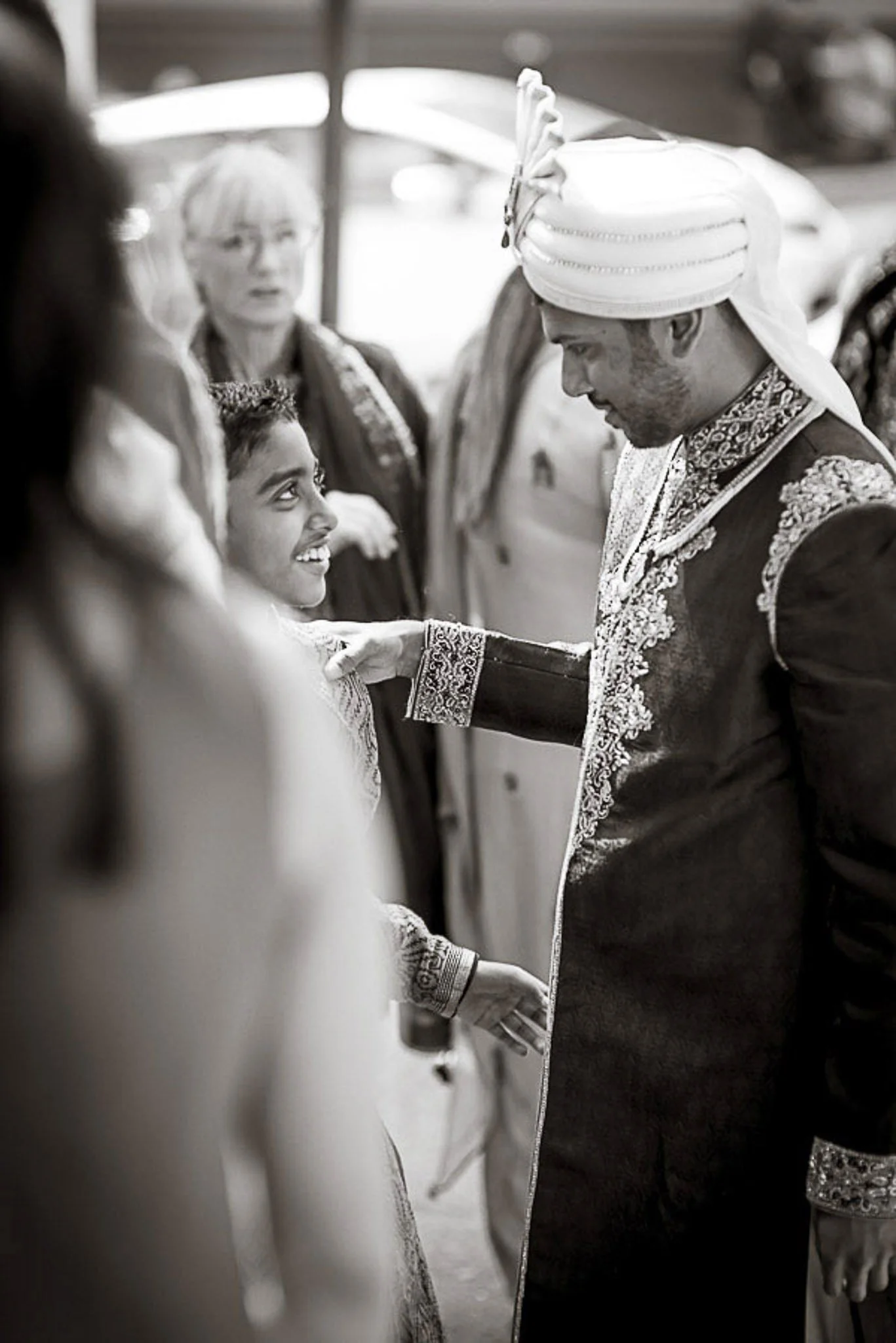 A groom and bride holding hands, dressed in traditional wedding attire, during a ceremony. The groom is wearing a turban and the bride is smiling up at him.