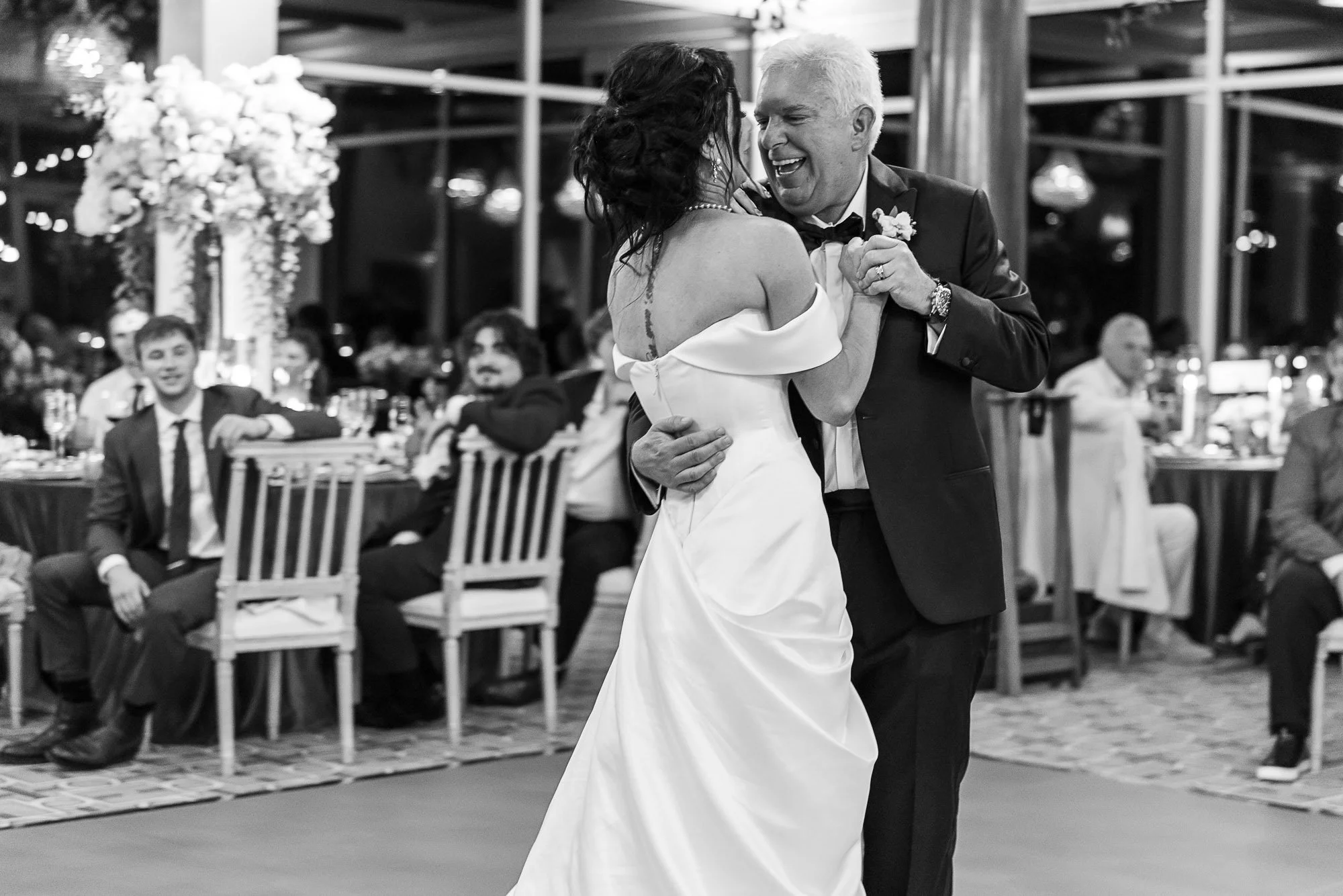 A bride and groom dance together at their wedding reception, with seated guests in the background, in an elegant indoor venue at the Beach and Tennis Club in Pebble Beach, CA.
