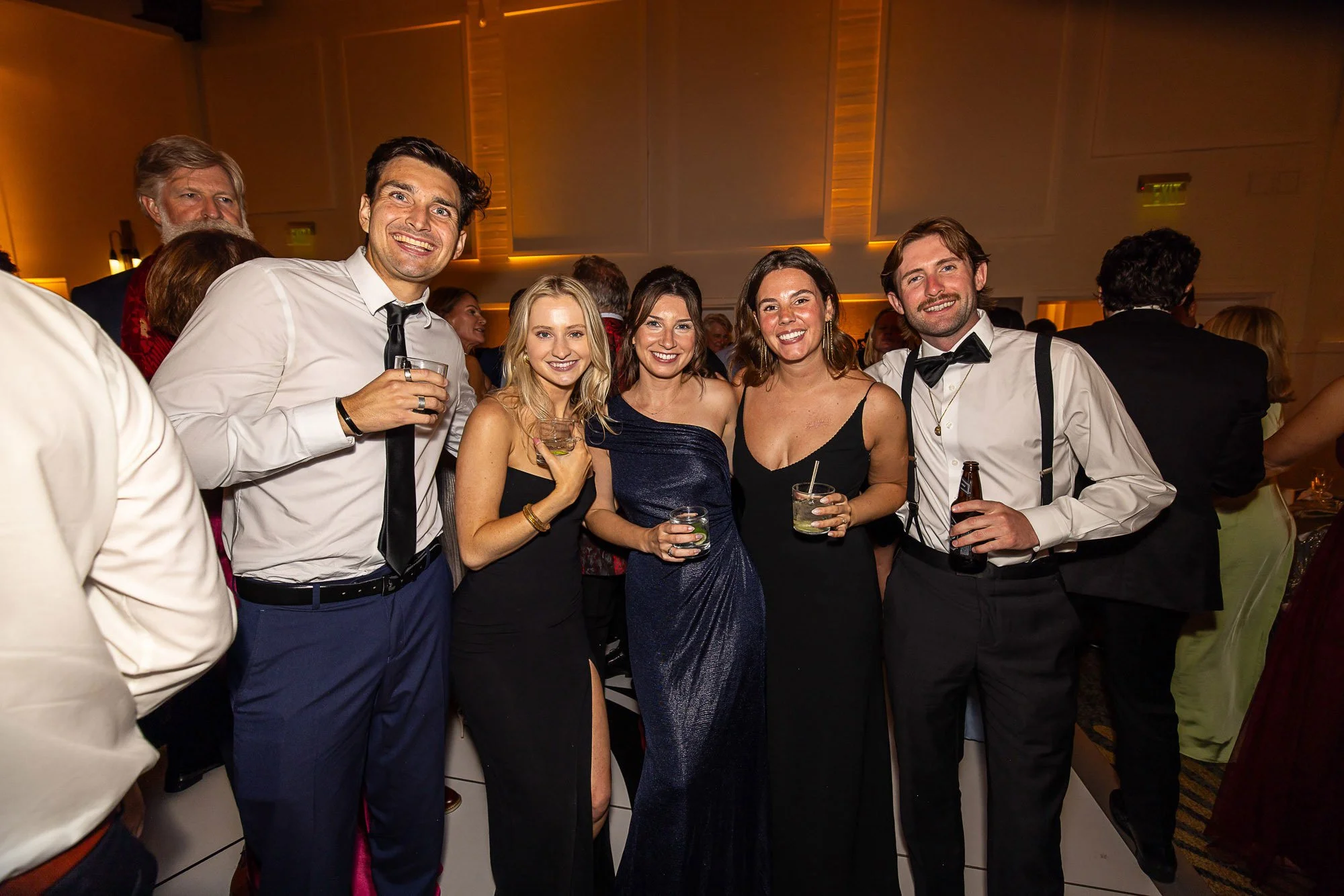 Group of five people dressed in formal attire at a party or celebration, smiling and posing for the camera, holding drinks at Cavallo Point in Sausalito, CA.