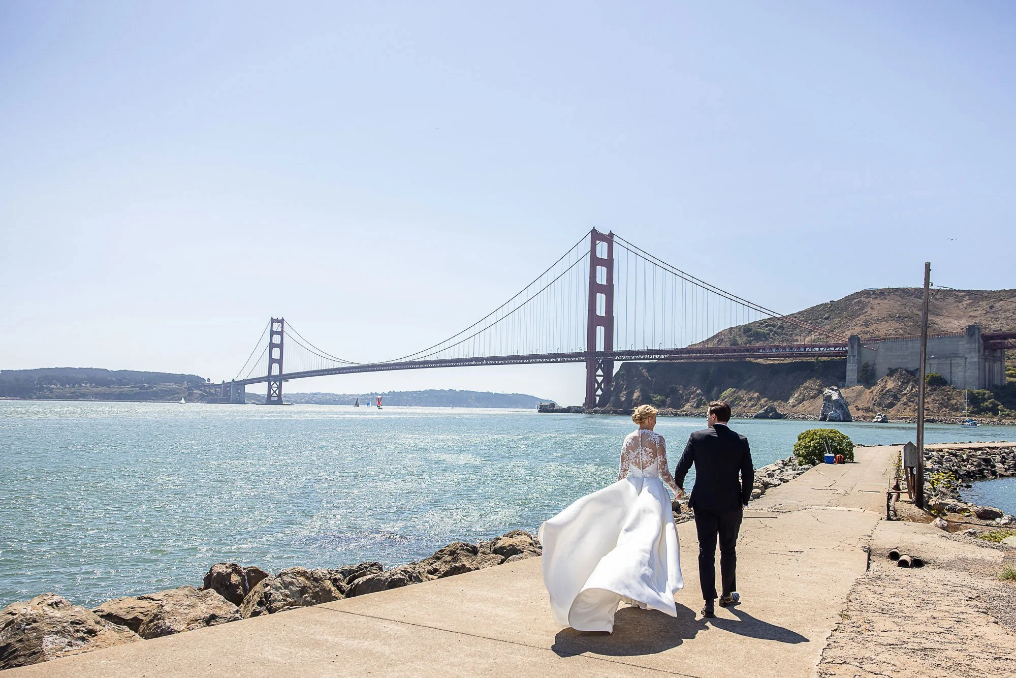 Bride and groom walking the pier at Cavallo Point with the Golden Gate Bridge behind them.