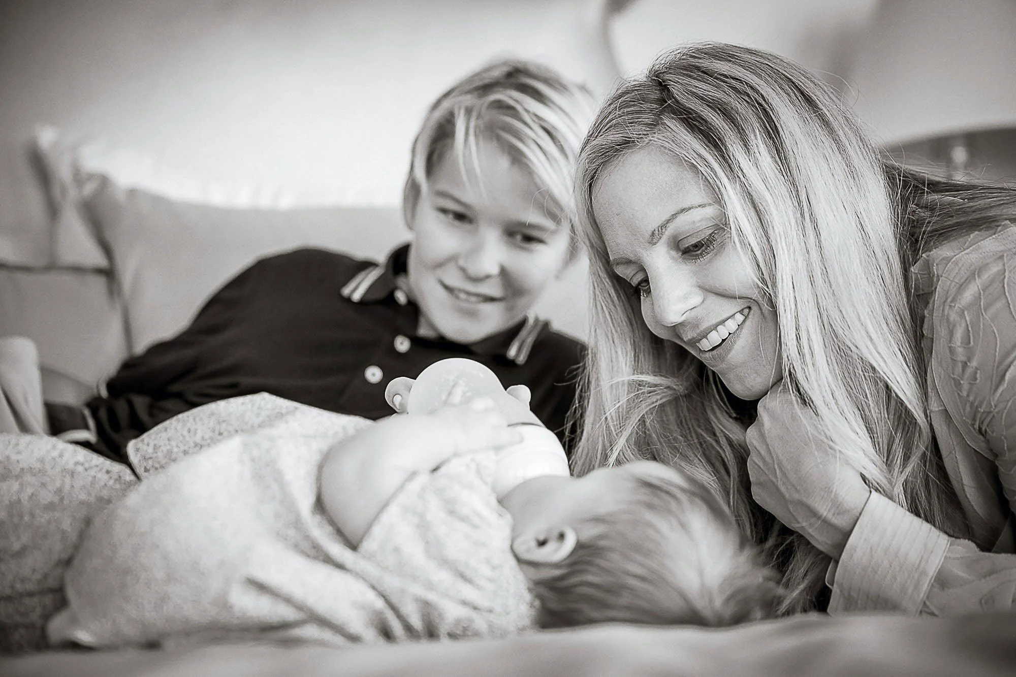 A woman and a young girl are smiling as they look at a baby lying in a crib. The scene is in black and white.