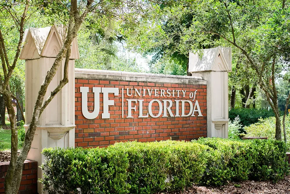 Brick University of Florida entrance sign surrounded by trees and greenery.