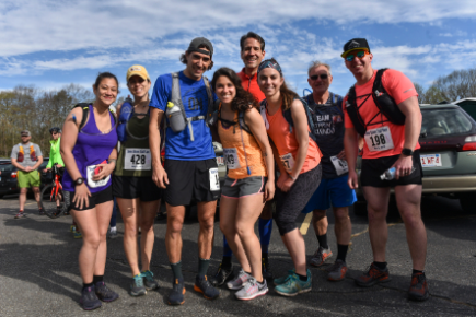 Group of eight runners in colorful athletic gear posing together outdoors during a mountain race event.
