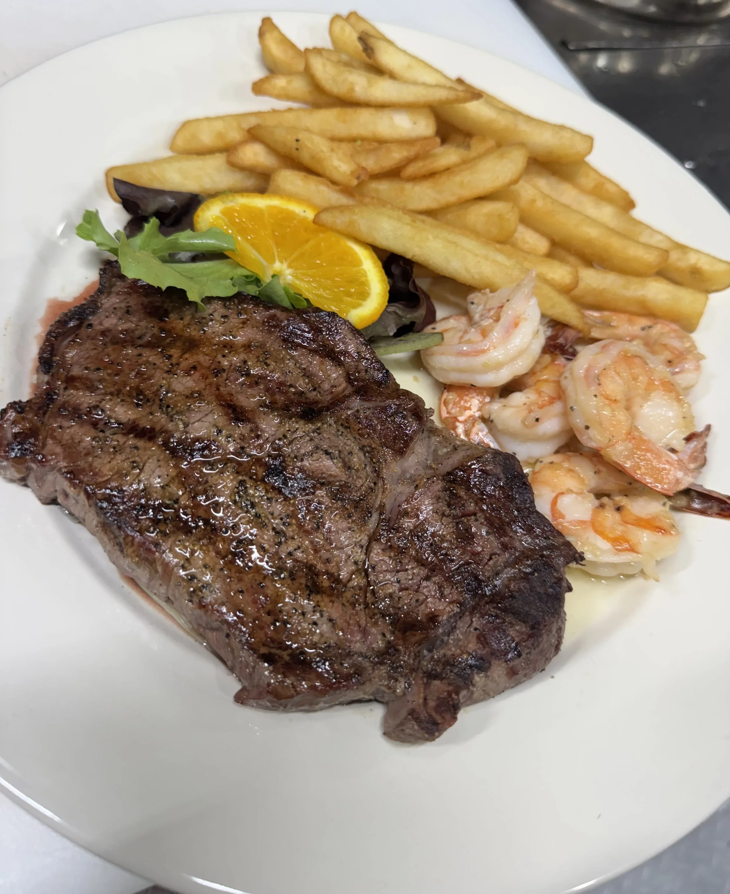 A plate of food with French fries, grilled sirloin steak, garlic butter shrimp, side salad.