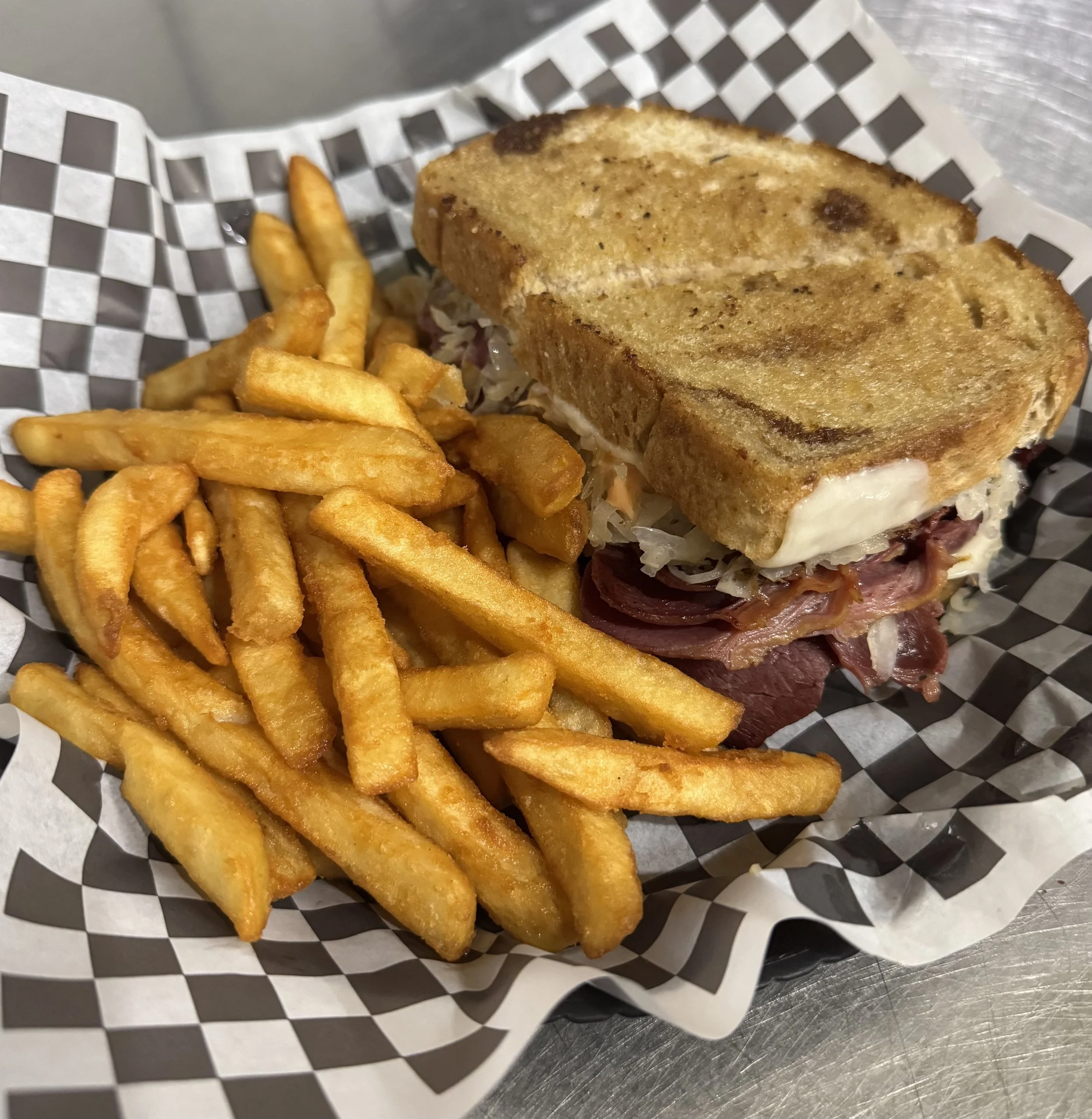 Golden French fries and a classic rueben sandwich with toasted bread, corned beef, and Swiss cheese in a checkered paper-lined basket.