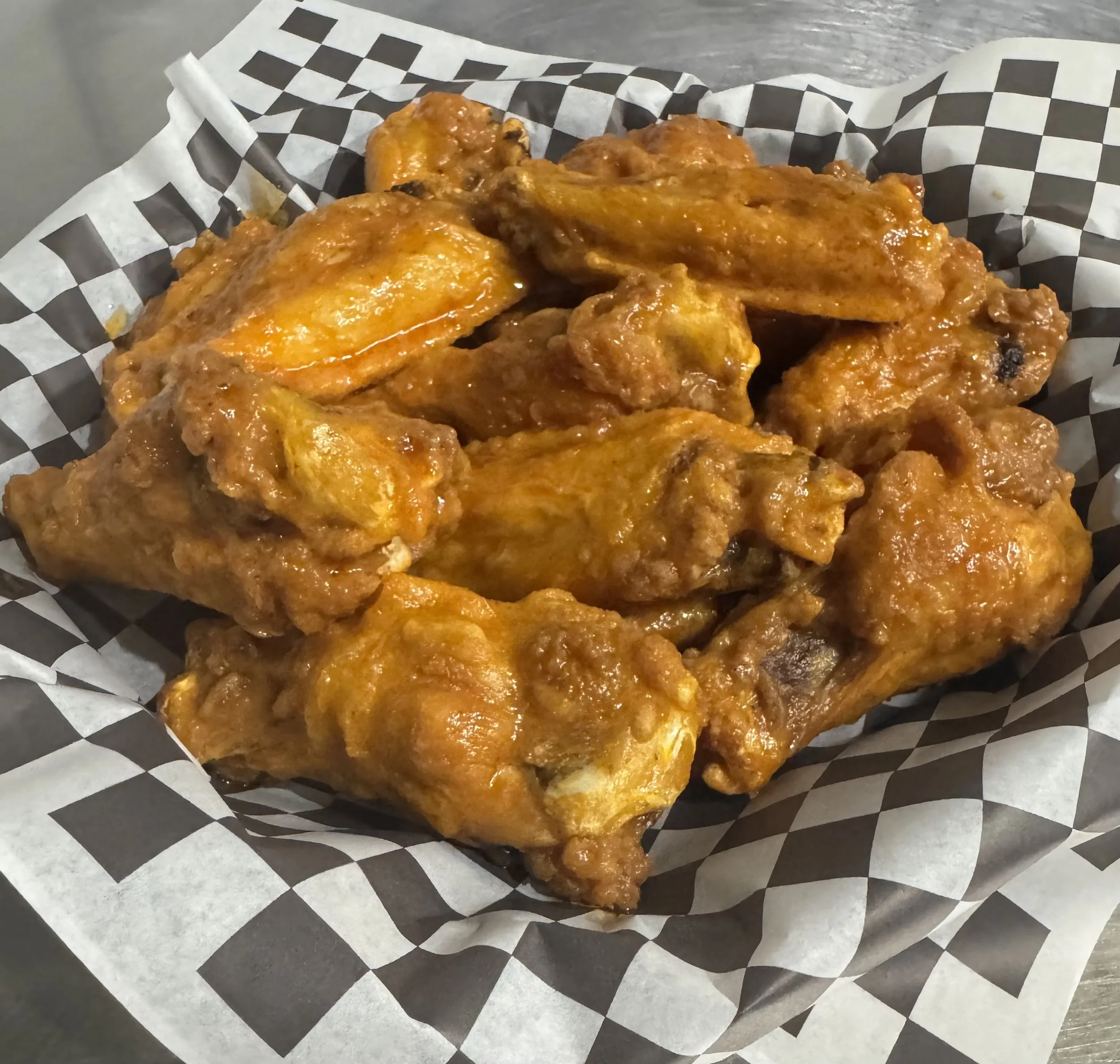 Close-up of dozen bone-in wings tossed in sauce placed on black and white checkered paper on a gray surface.