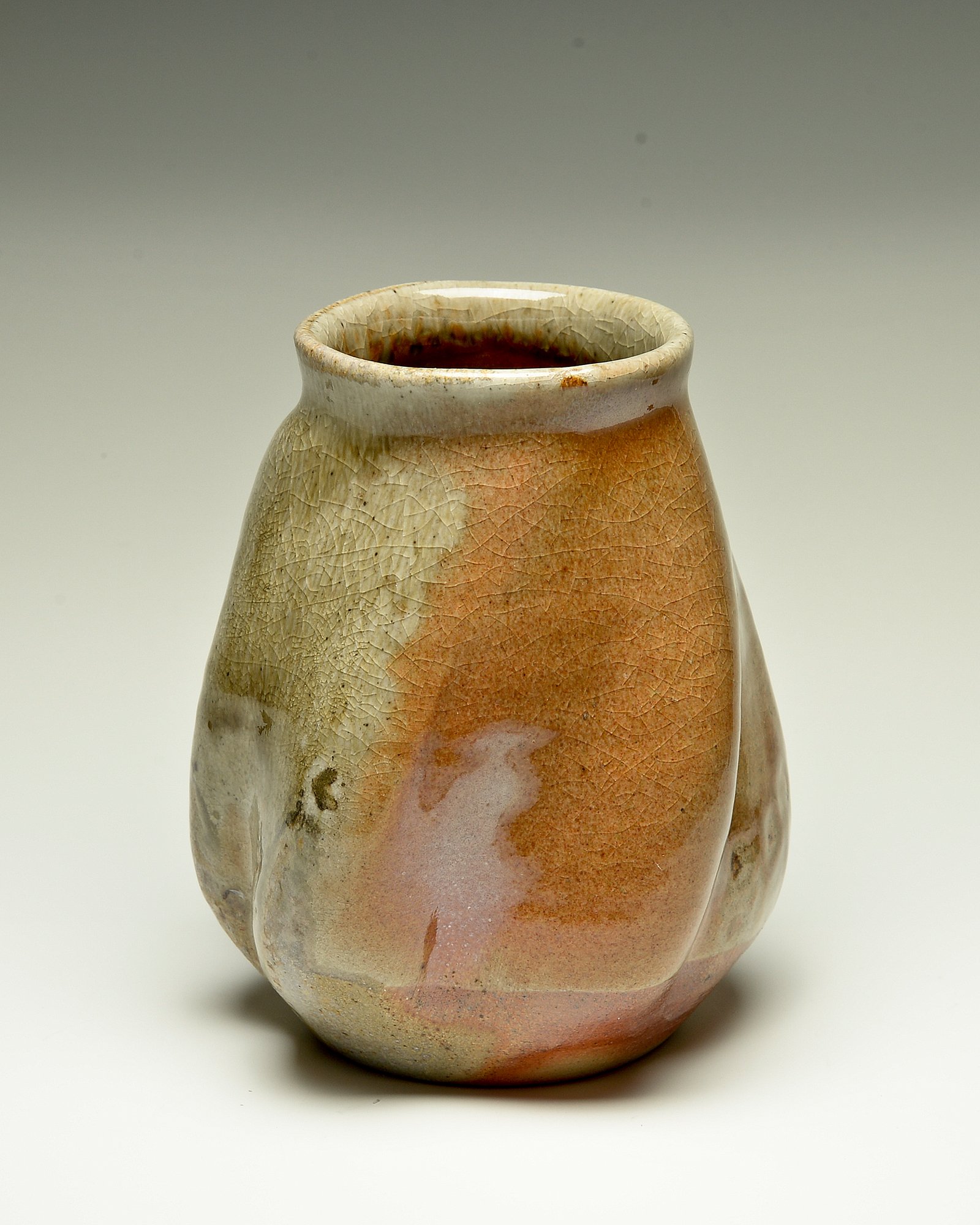 A ceramic vessel with a wide opening, glazed in earthy tones of beige, pink, and brown, featuring a crackled glaze pattern and smooth, rounded shape.