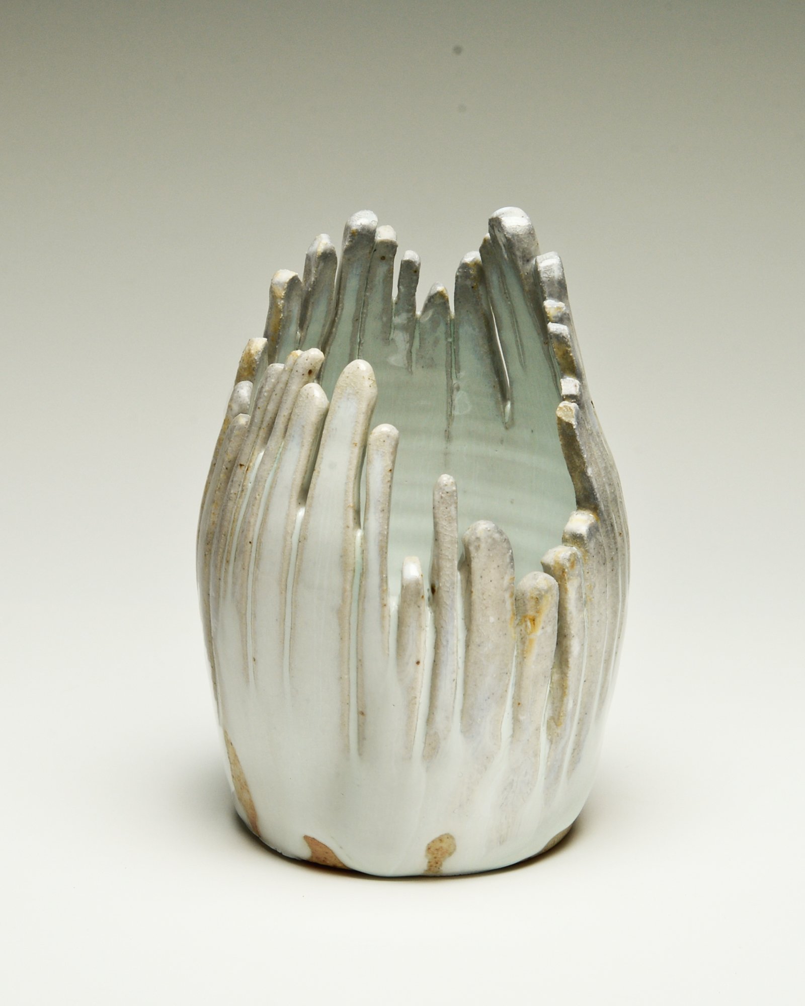 A ceramic vase with a white glaze finish, featuring a textured surface with vertical ridges and a slightly irregular shape.