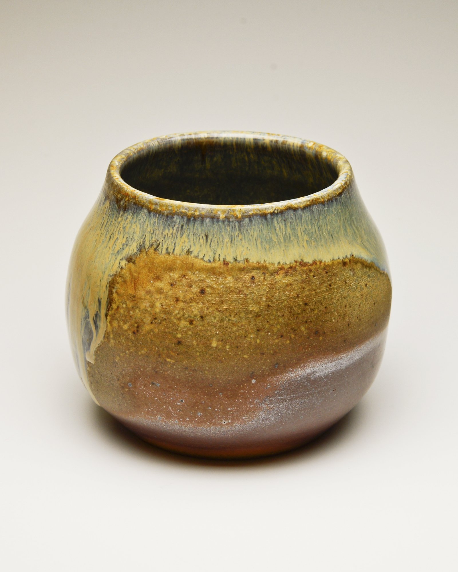 Close-up of a textured ceramic vase with earthy tones and gradient glaze, against a plain white background.