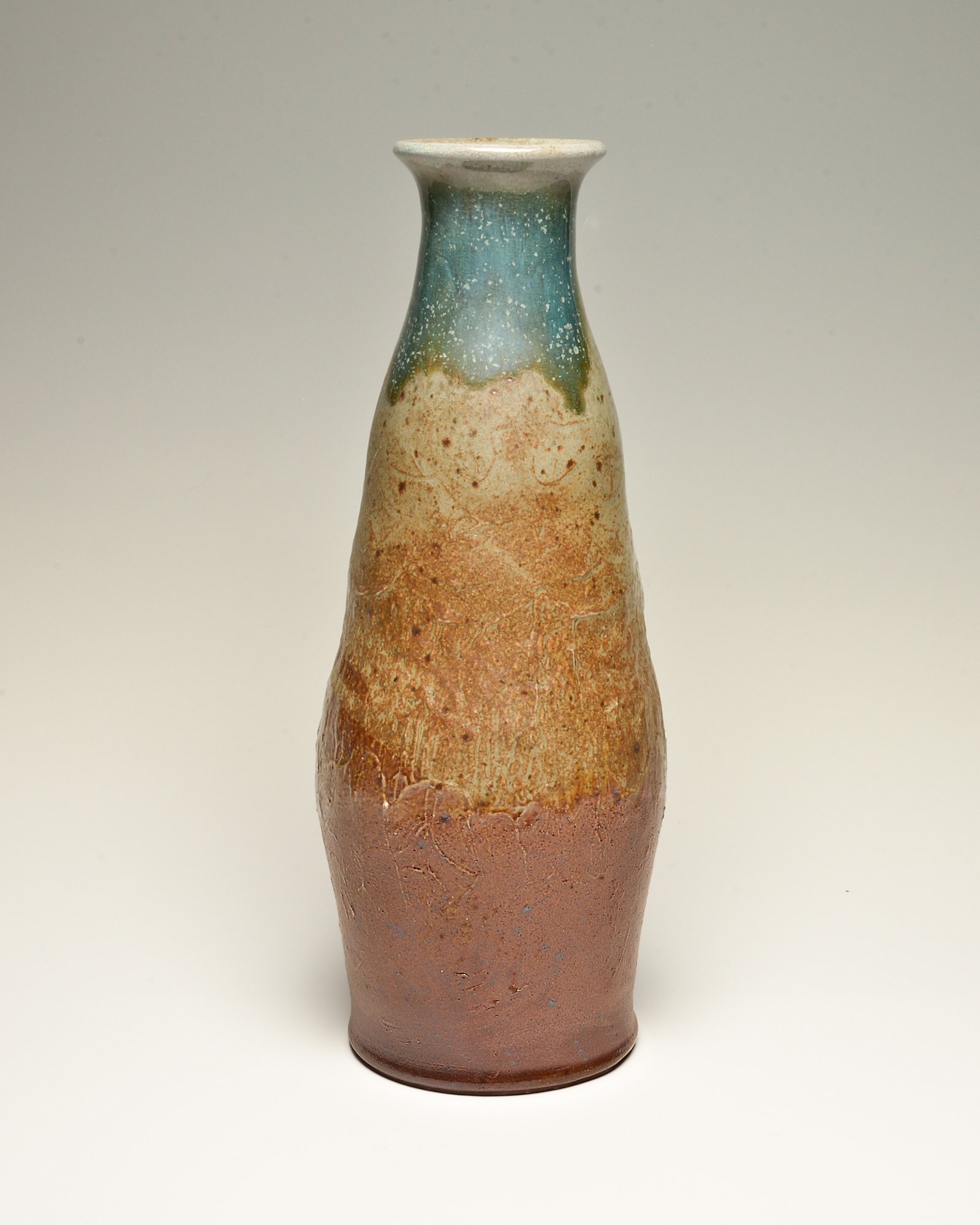 A ceramic vase with a narrow base, wider middle, and a flared top, featuring a gradient glaze from reddish-brown at the bottom to a speckled blue-green at the top.