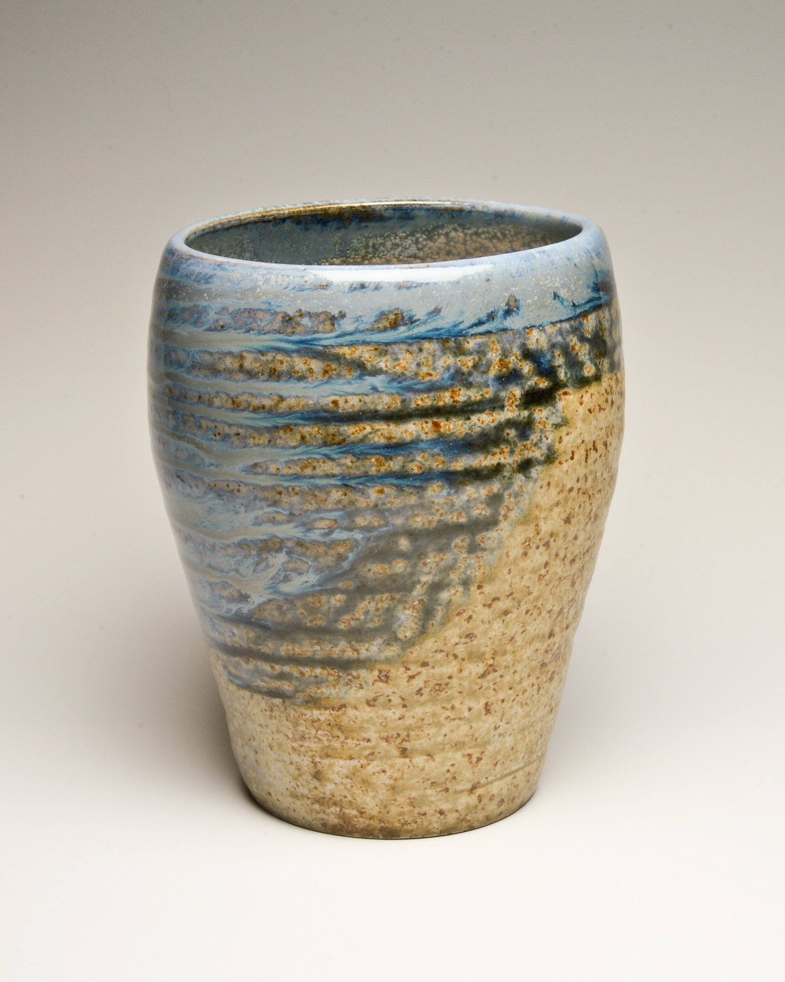 A ceramic vase with a textured, wavy pattern in blue, beige, and brown tones, set against a plain background.