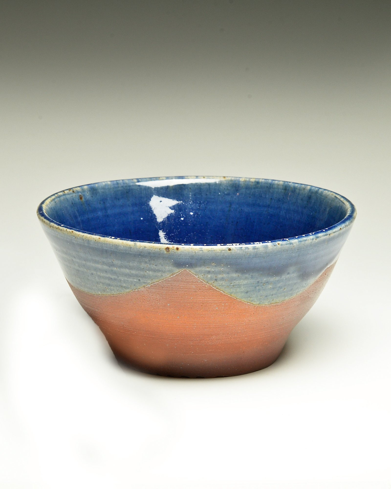 A ceramic bowl with a blue glaze interior and a pinkish-orange exterior, set against a white background.