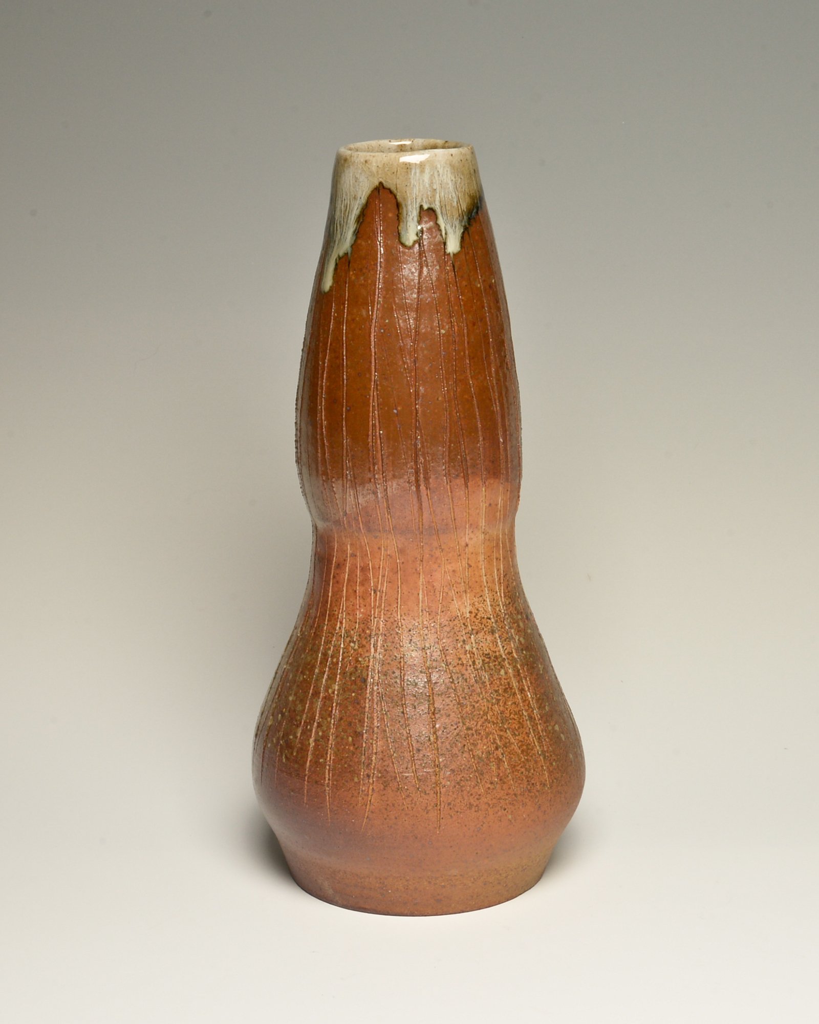 Ceramic vase with a narrow neck, reddish-brown color, textured surface, and cream-colored dripping glaze at the top.