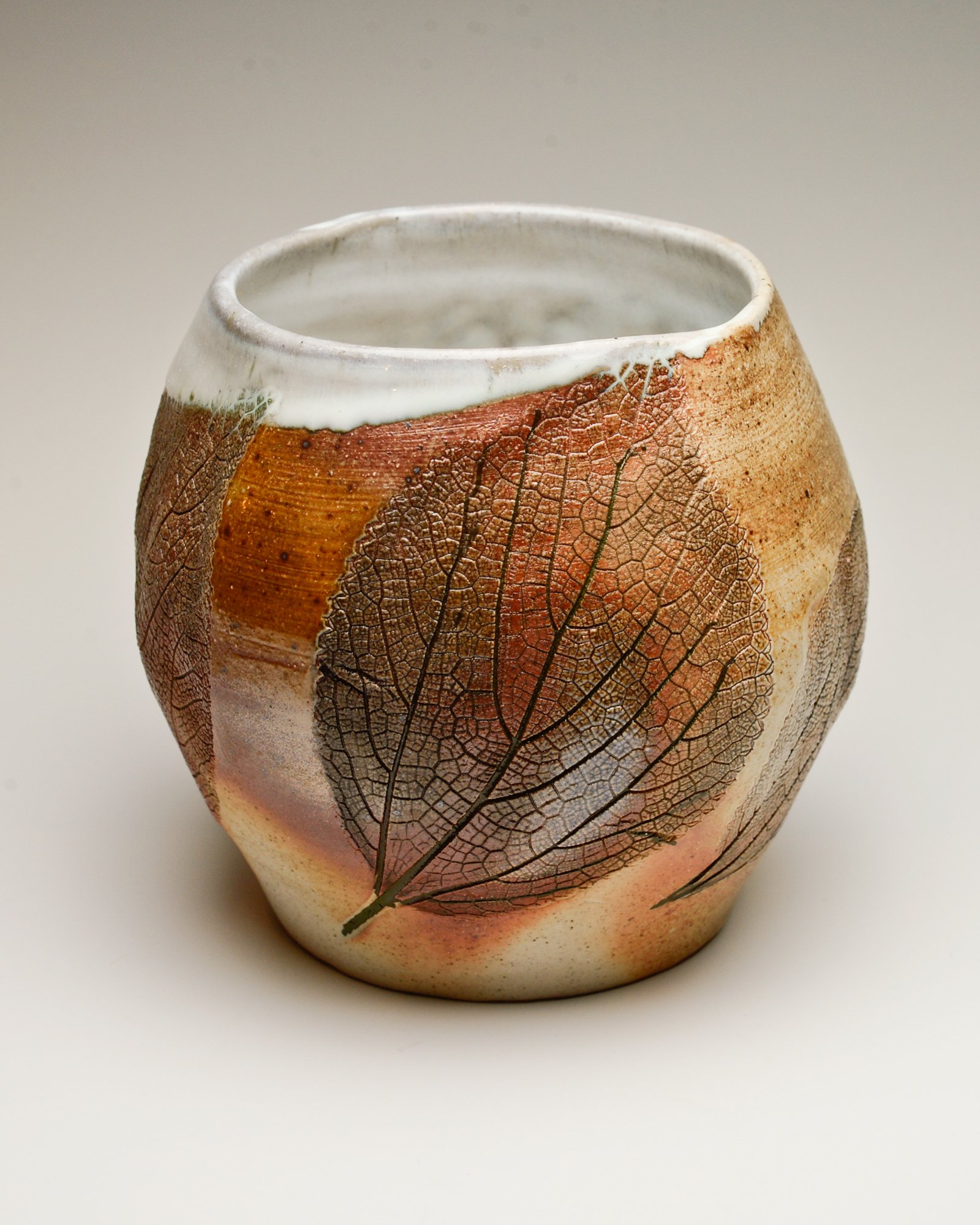 A ceramic vase with a leaf pattern featuring detailed veins and autumn colors.