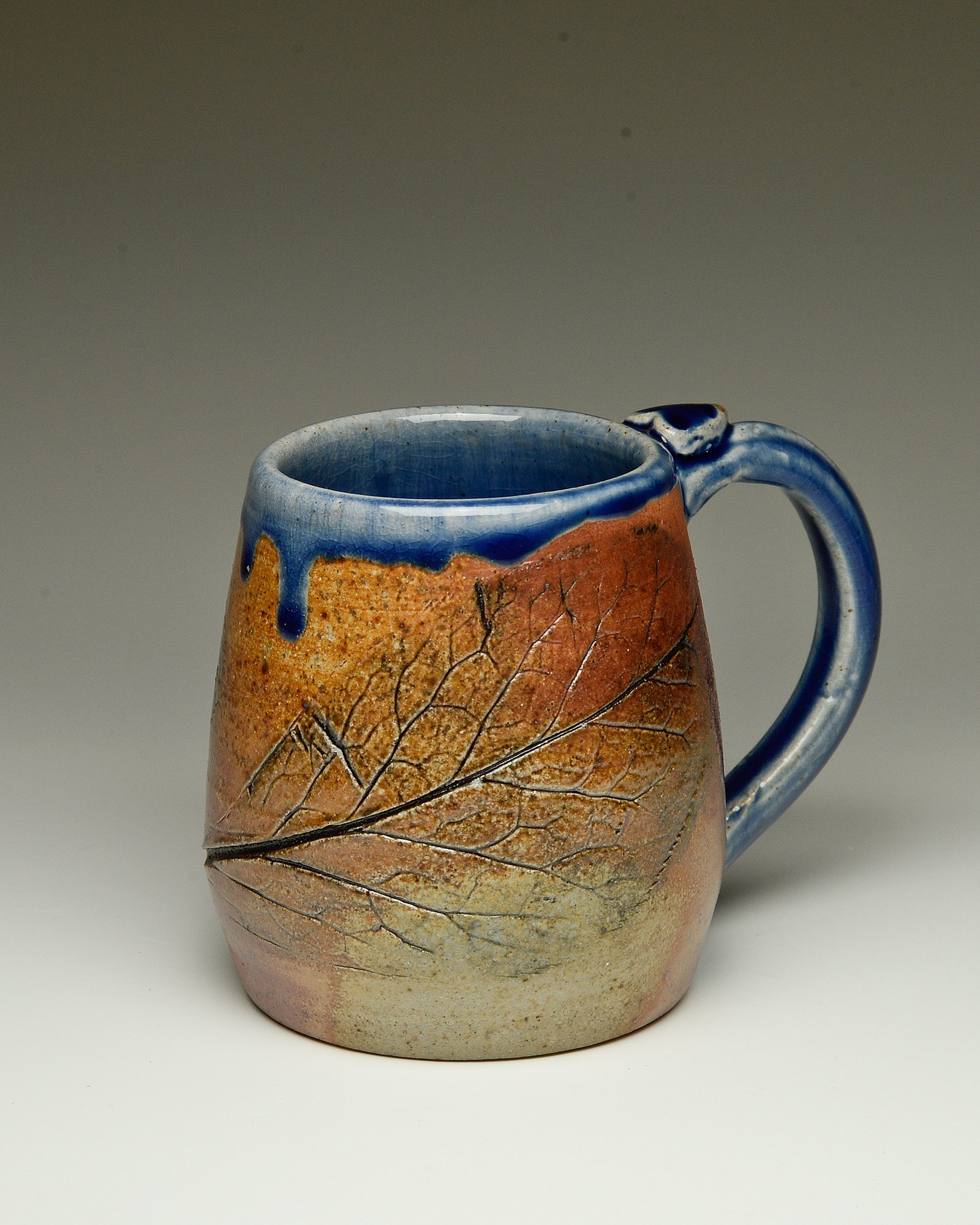 Ceramic mug with a textured, cracked surface, blue glaze dripping from the lip, and a deep handle, on a neutral background.