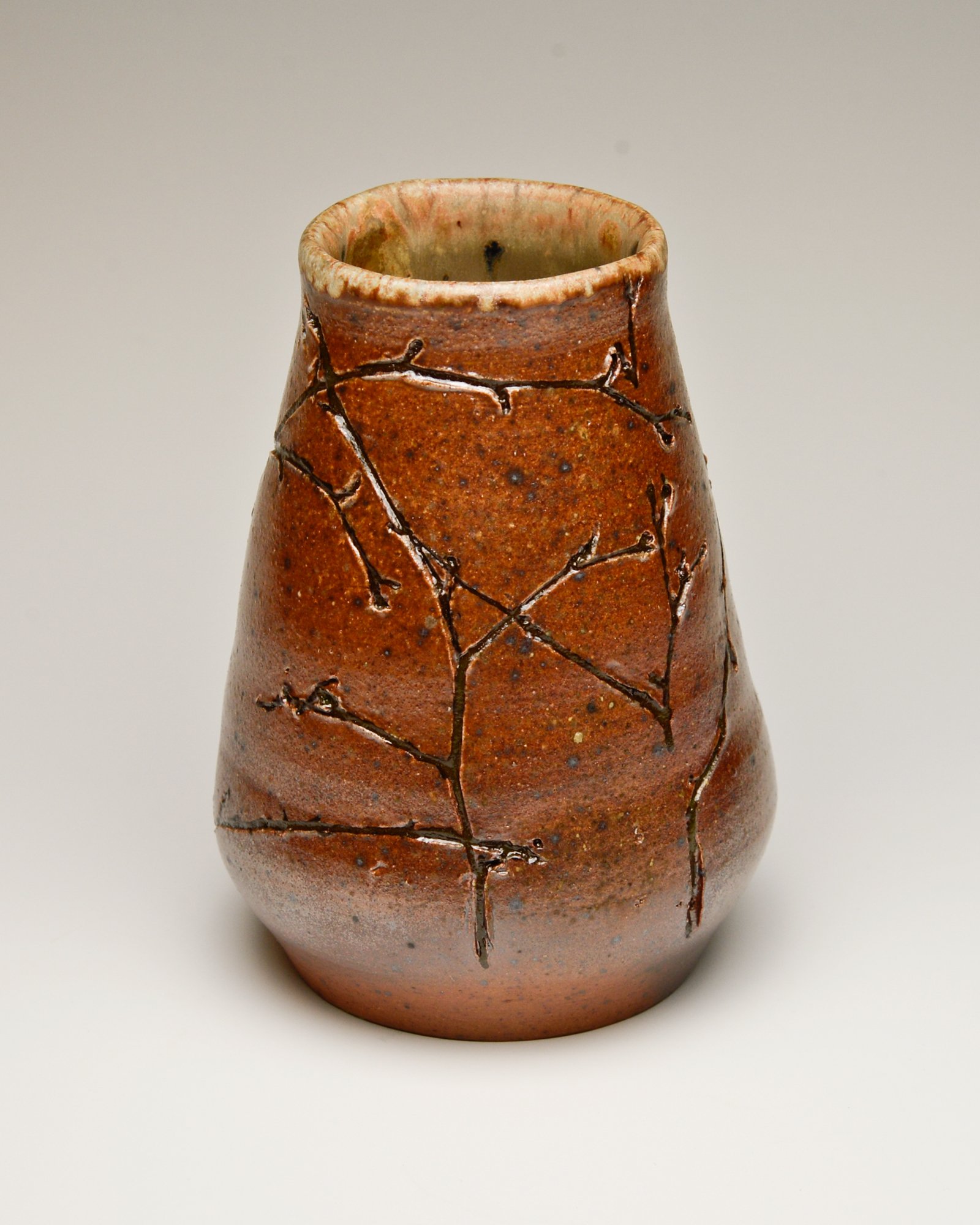 A ceramic vase with a reddish-brown glaze and a textured surface, featuring black crackle patterns.