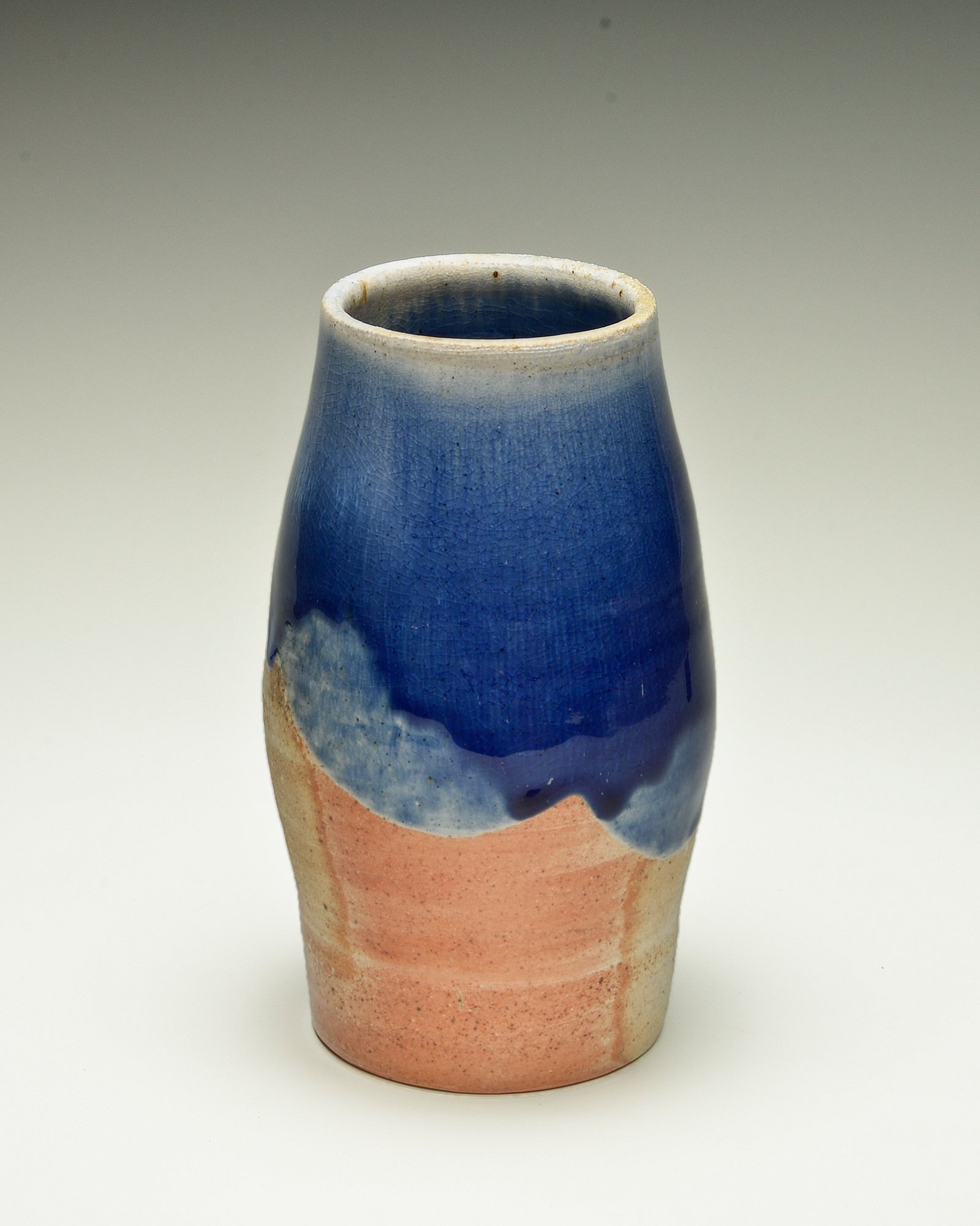 A ceramic vase with a pinkish base and a blue glaze at the top, featuring a crackled texture and artistic drips.