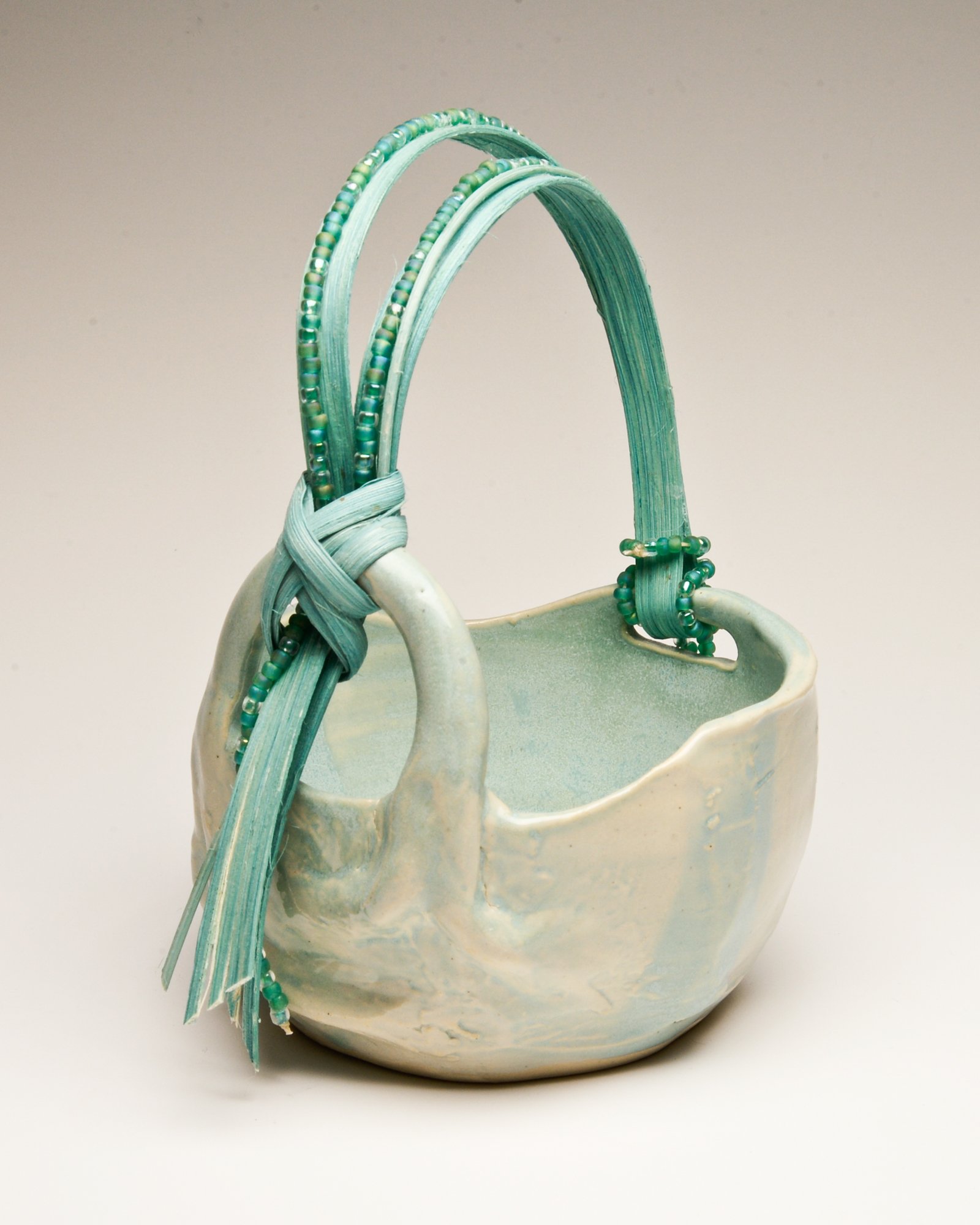 A ceramic vase with a light glaze, holding dried green and beige plant stems decorated with small beads and beads. The vase has a rustic, handmade appearance.