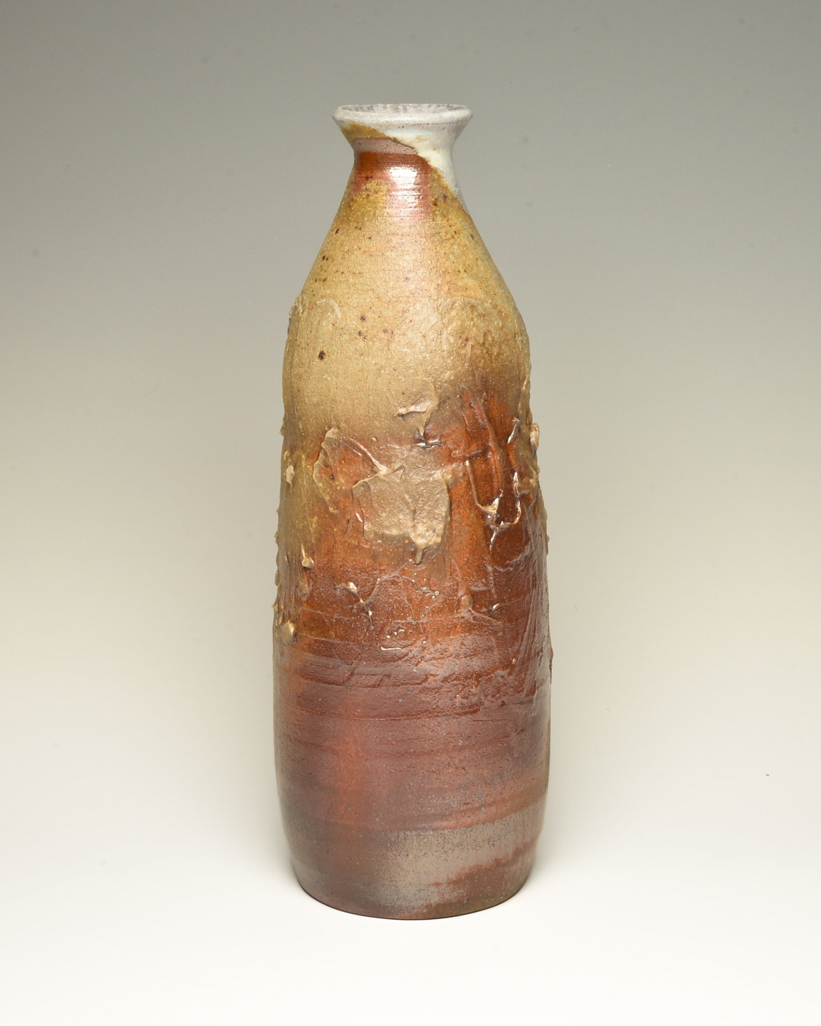 A tall ceramic vase with a narrow neck and wider base, featuring a textured, earthy glaze with reddish-brown, beige, and white tones.