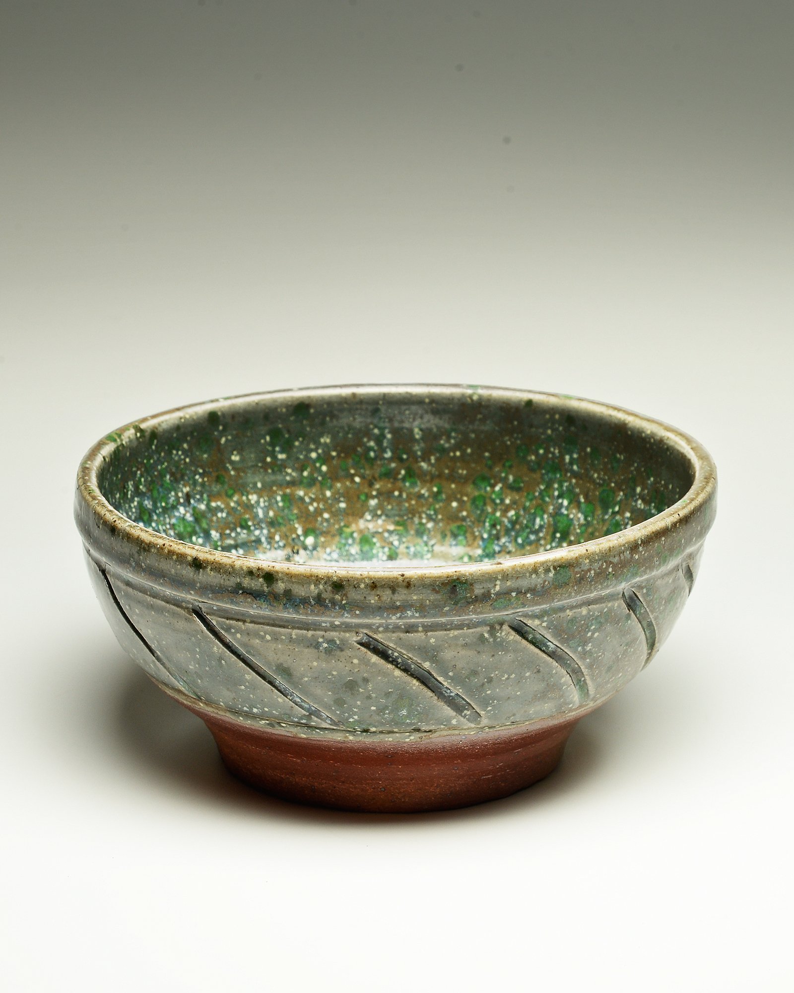 A ceramic bowl with a textured, multicolored glaze interior and a red base, shown against a plain white background.