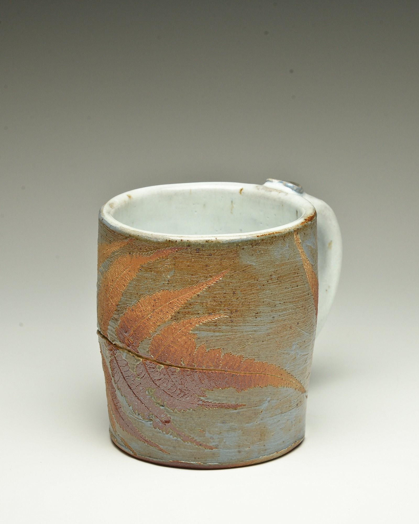 A ceramic mug with a textured, earth-tone design and a white interior, shown against a plain background.