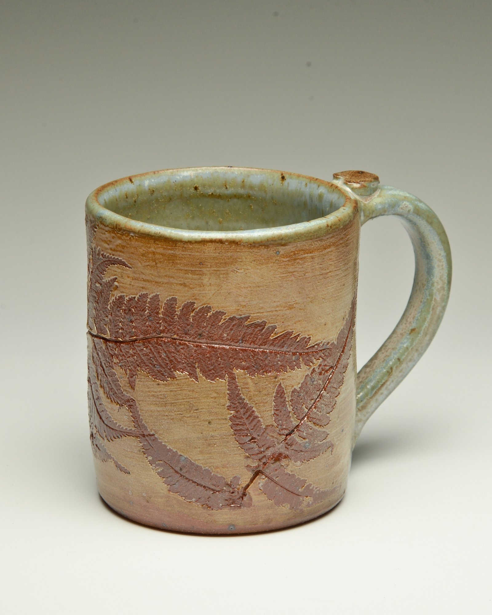 A ceramic mug with a textured, earthy design featuring leaf patterns and a glazed interior, set against a plain background.