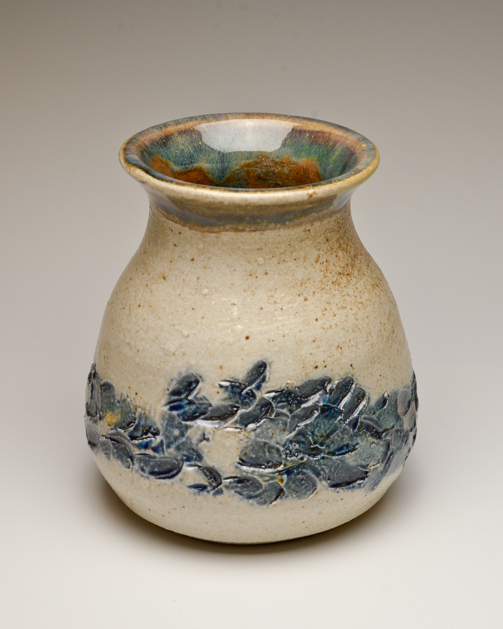 A ceramic vase with a textured and multicolored glaze finish, featuring a wide neck and a rounded body, decorated with abstract blue and black design elements.