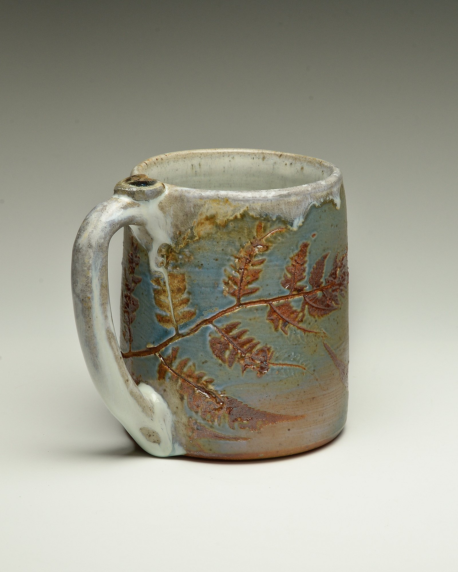 Handmade ceramic mug with a leaf motif and textured glaze.