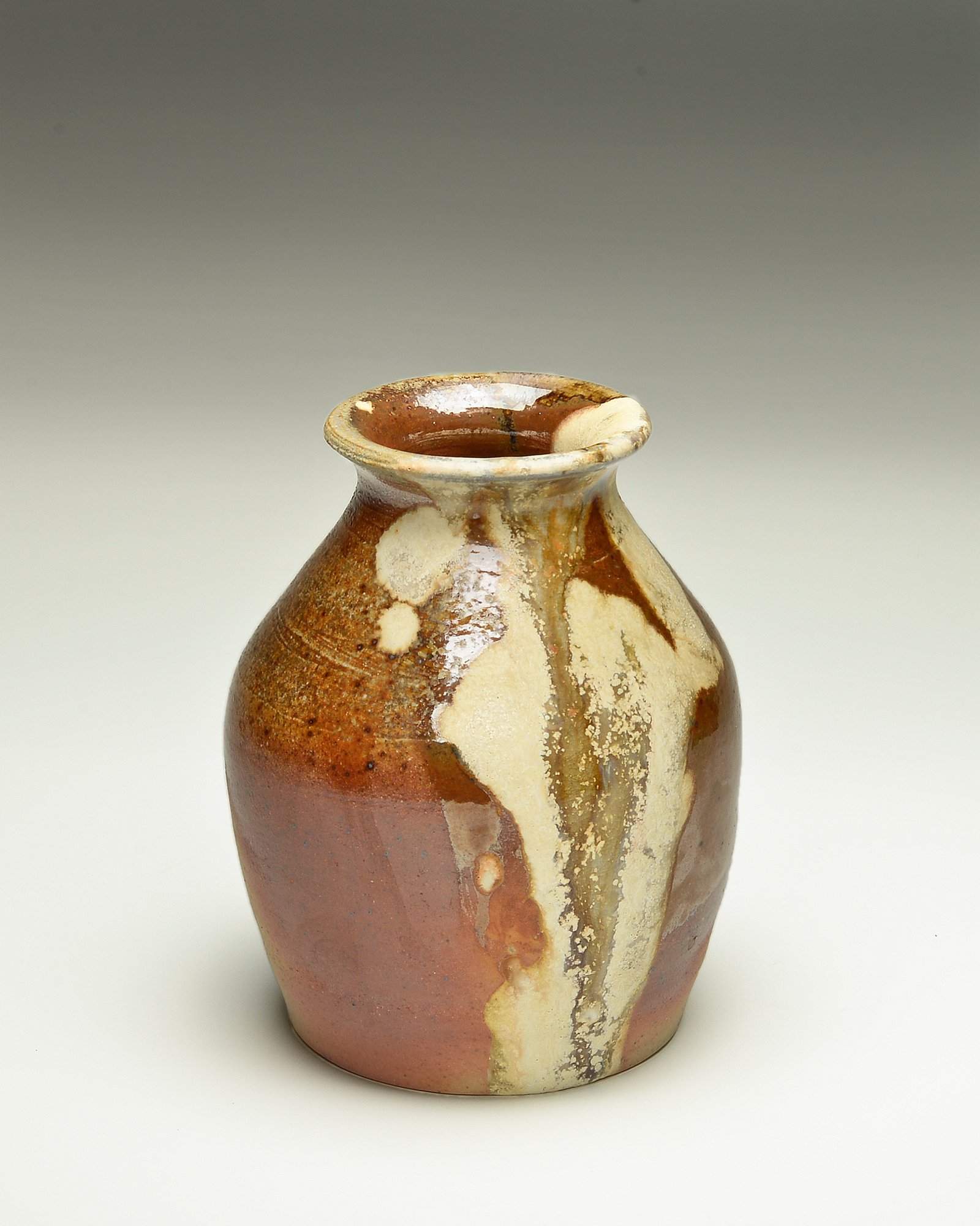 A ceramic vase with a narrow neck and rounded body, decorated with a glaze of brown, cream, and beige colors with flowing patterns.