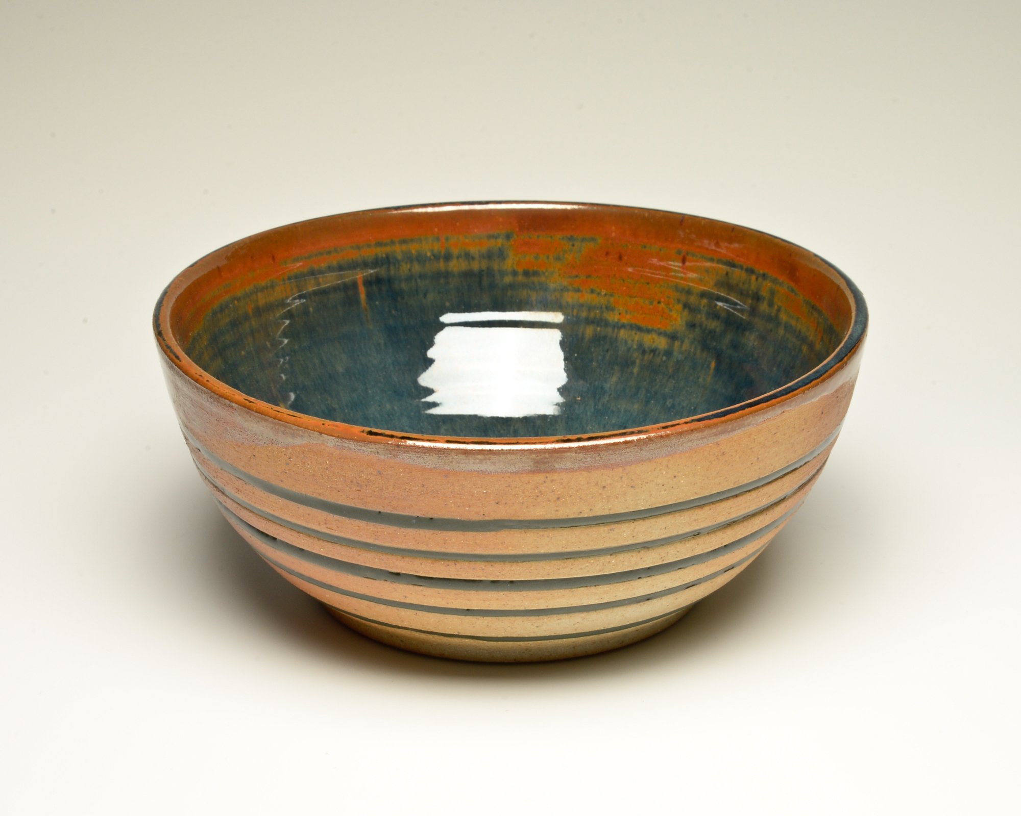 Stacked ceramic bowls with a reddish exterior and a blue-green interior, placed on a white surface.