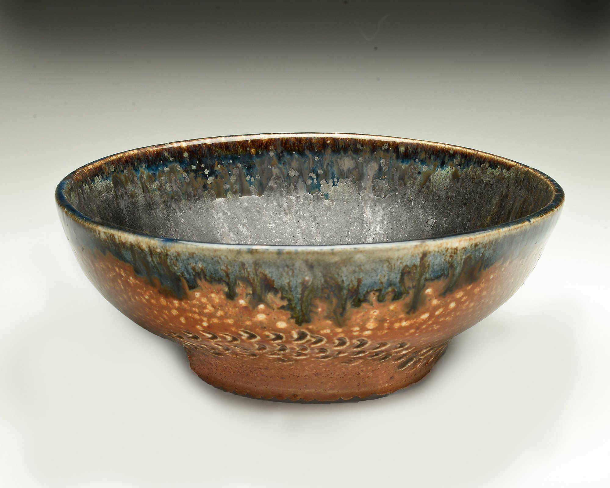 A handmade ceramic bowl with a textured bottom, decorated with blue, brown, and black glaze, filled with white salt.