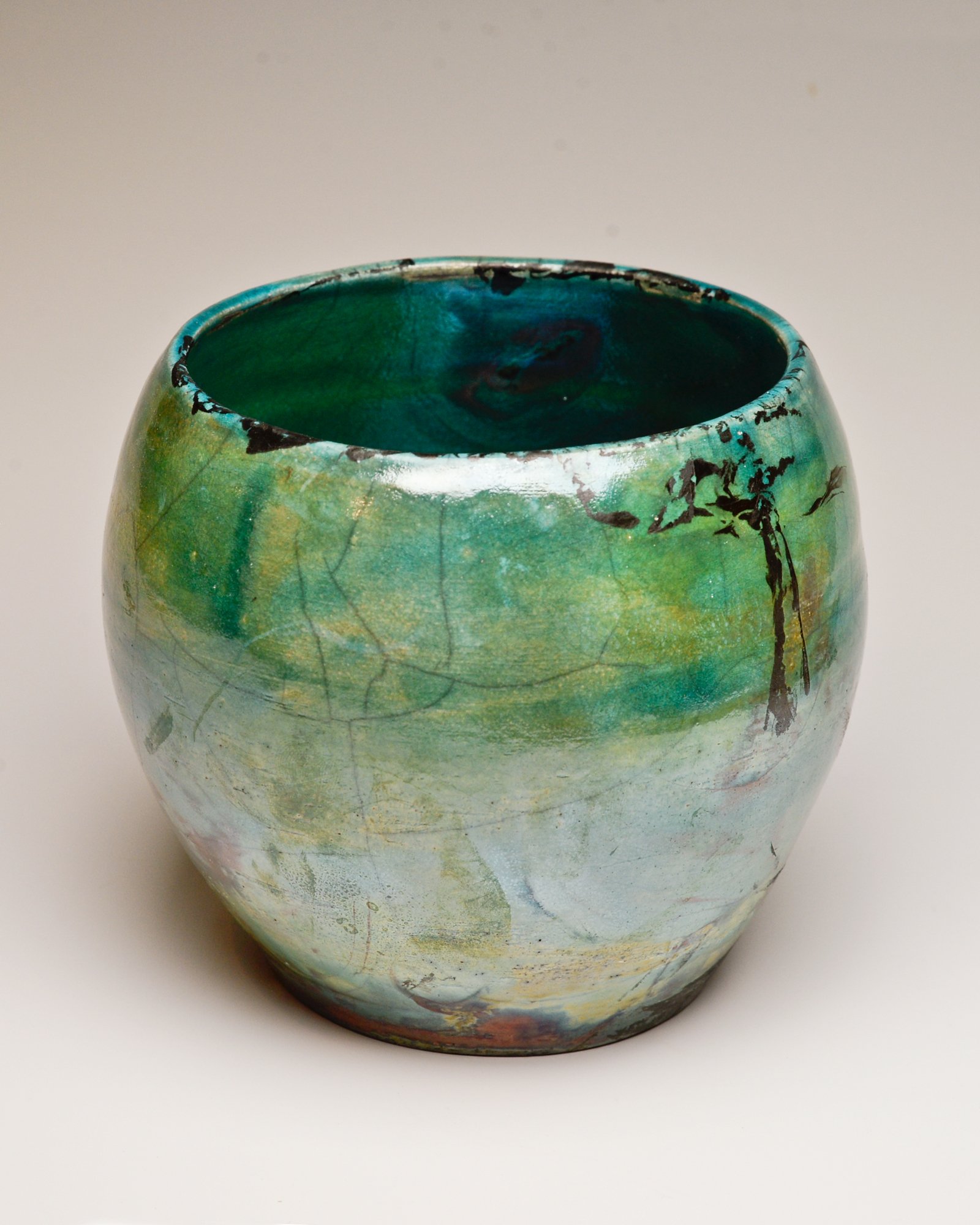 A ceramic vase with a green and blue glaze, black crackle pattern, and some black paint splashes, against a plain white background.