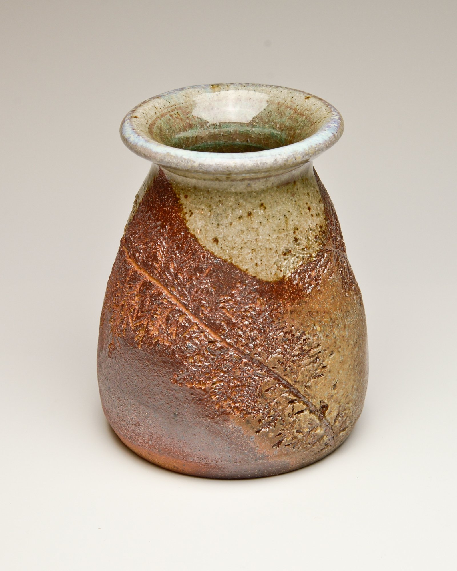 A ceramic vase with a wide opening and a textured, earthy surface, featuring a leaf pattern carved into the lower half.