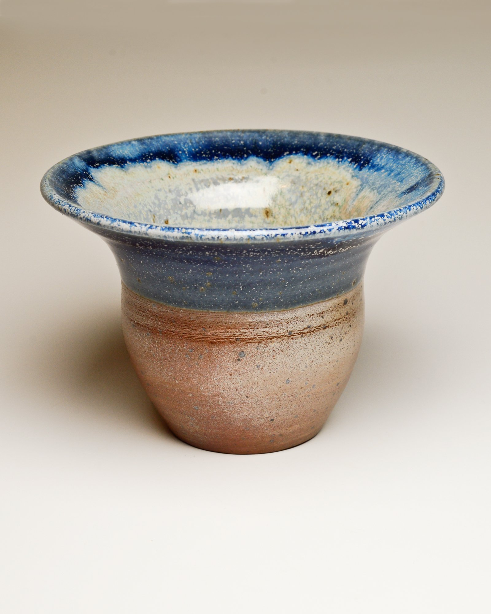 A ceramic vase with a wide blue-rimmed top, beige and brown gradient body, and a textured matte surface.