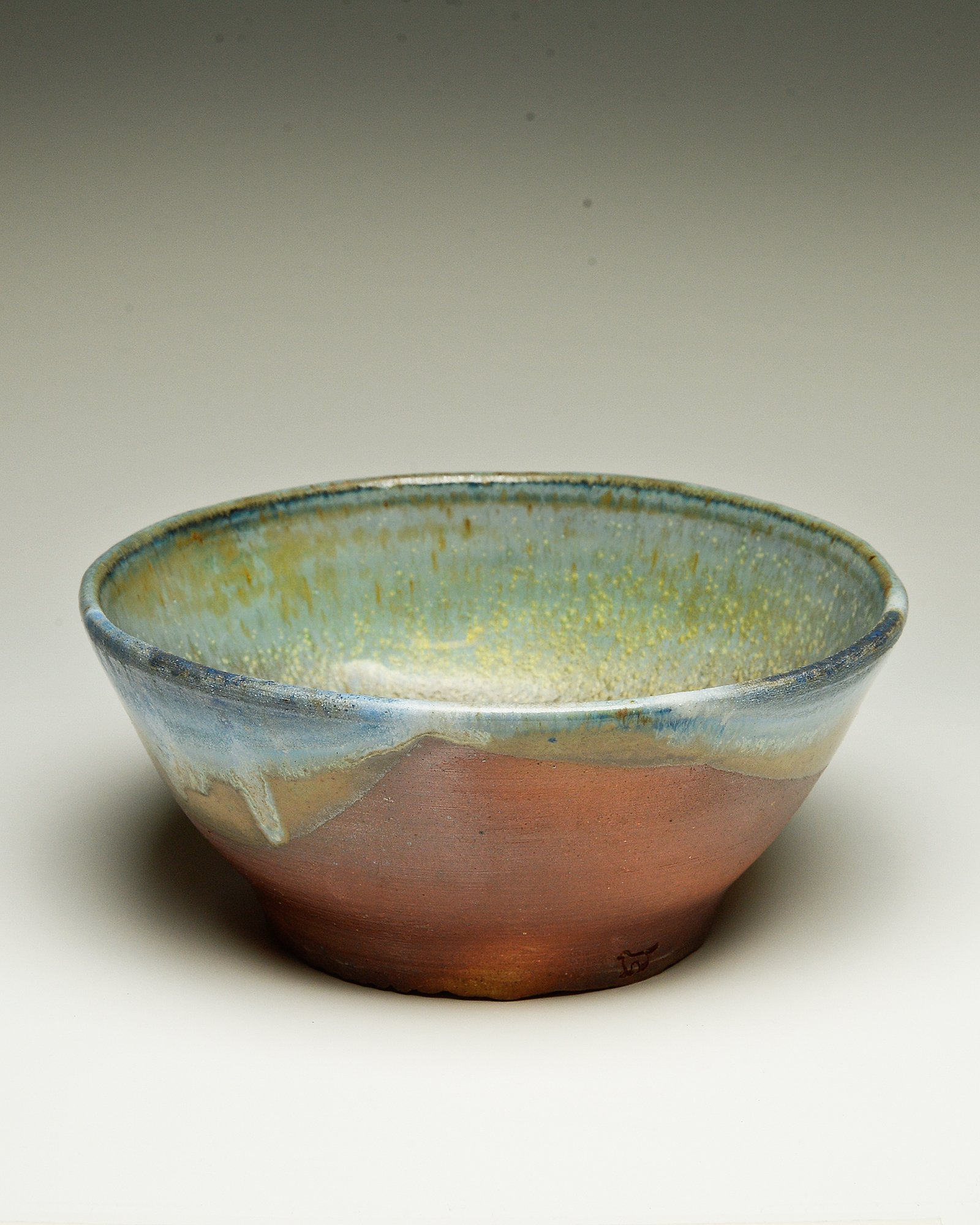 A ceramic bowl with a textured, multicolored glaze, earthy tones, and a decorative logo on the exterior.