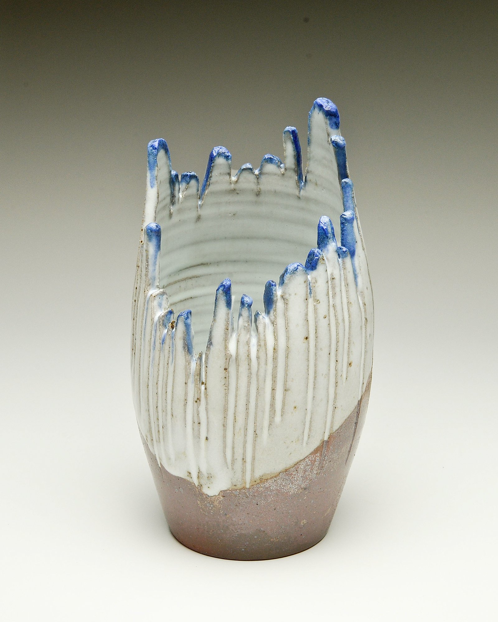 A ceramic vase with a textured, ridged surface and blue-tipped white glaze, tapering to a rounded base.