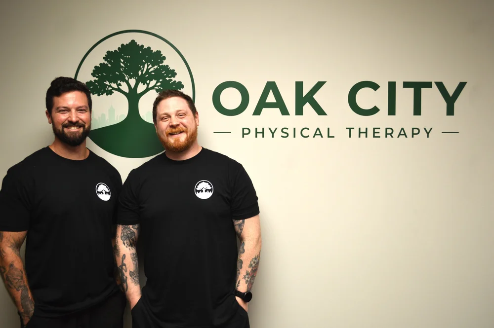 Oak City Physical Therapy co-founders Trevor Lewis and DJ Redmond standing in front of the clinic logo