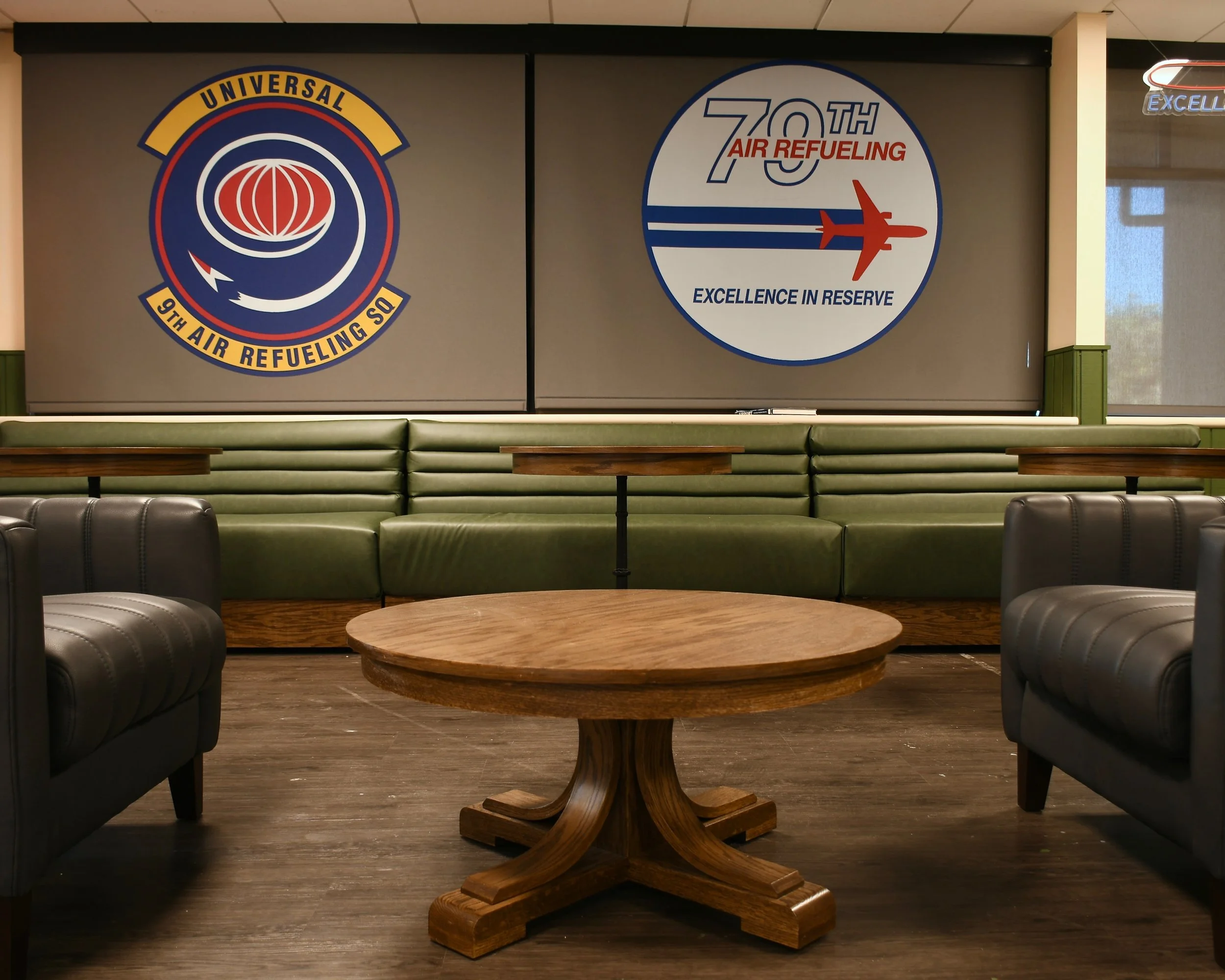 Decorative wall with 75th anniversary logos of Universal Air ReFueling, featuring an airplane and aviation-themed design, in an airport lounge with green cushioned seating and a round wooden table.
