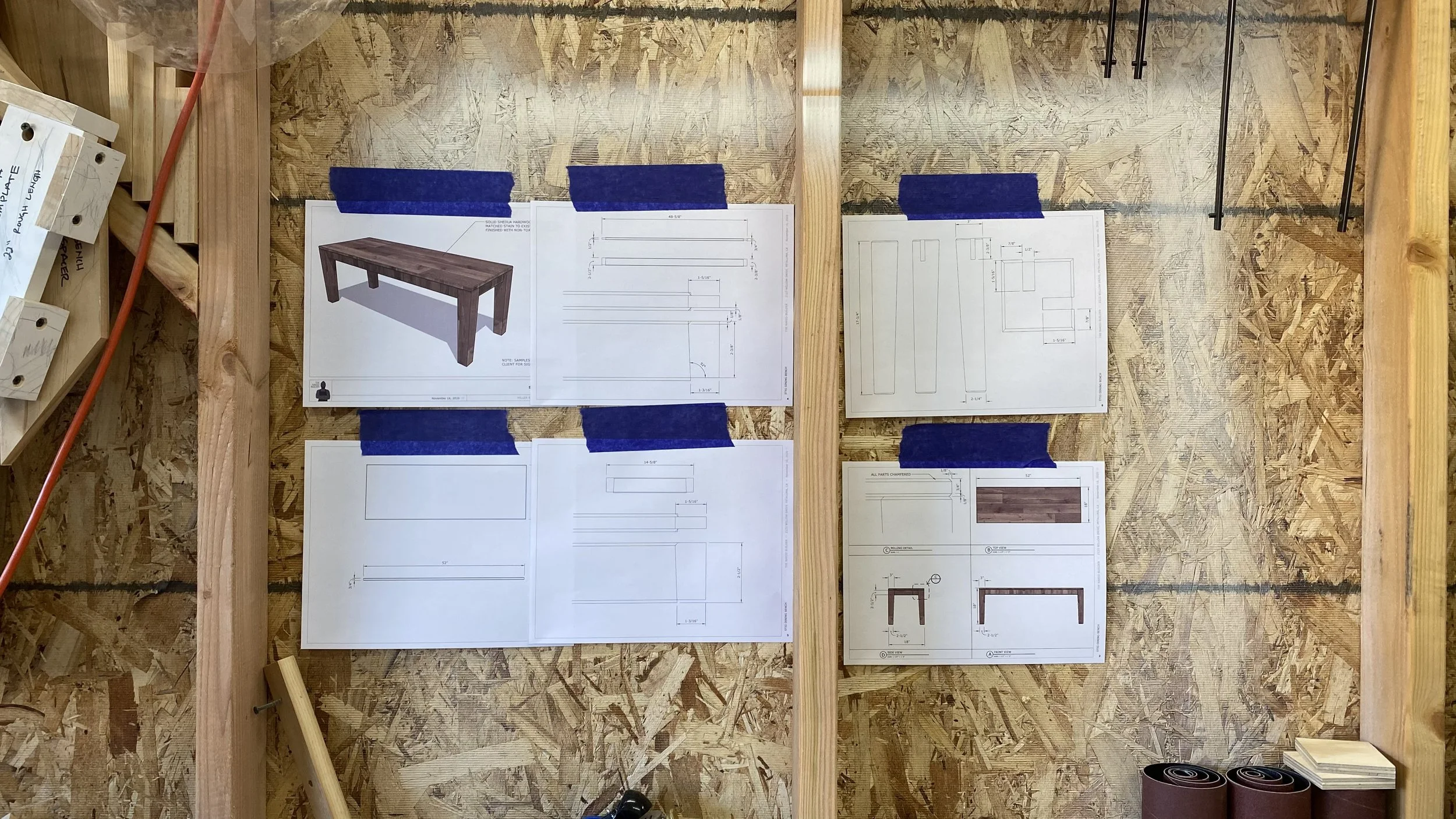 Blueprints and design plans for a wooden table attached to a wooden wall in a workshop.