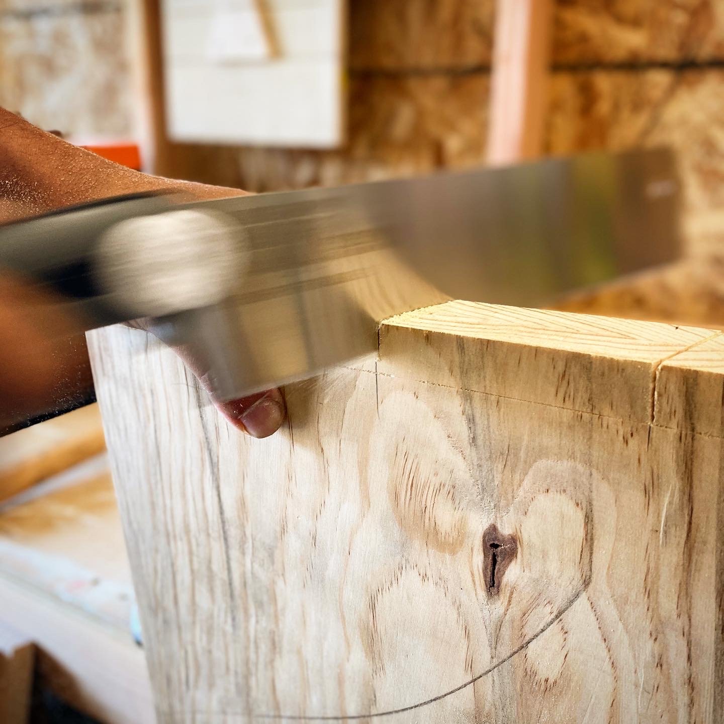 Close-up of a hand with a knife cutting into a wooden block in a woodworking shop.