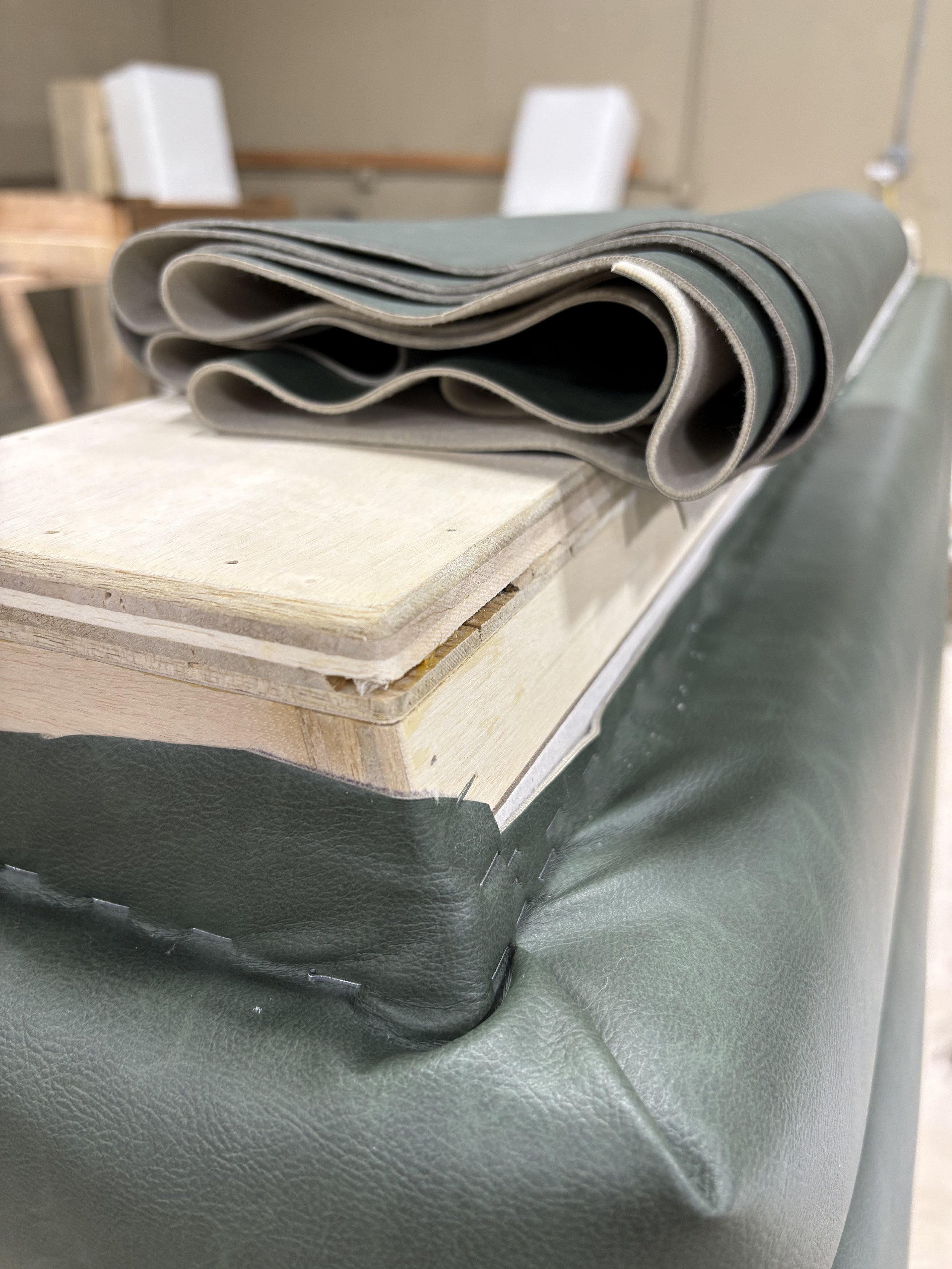 Several rolled-up fabrics or materials placed on top of a wooden board, situated on a dark green surface in a workspace or workshop.
