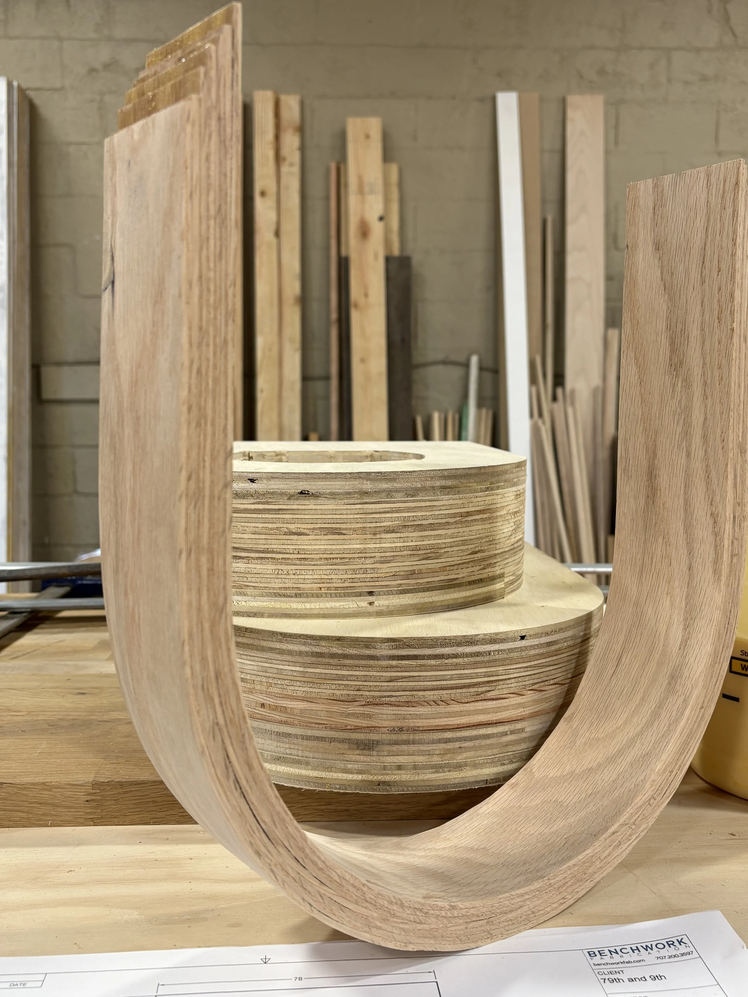 Wooden furniture piece in progress with curved and flat wooden panels, likely for a craft or furniture project, set against an indoor workshop background.