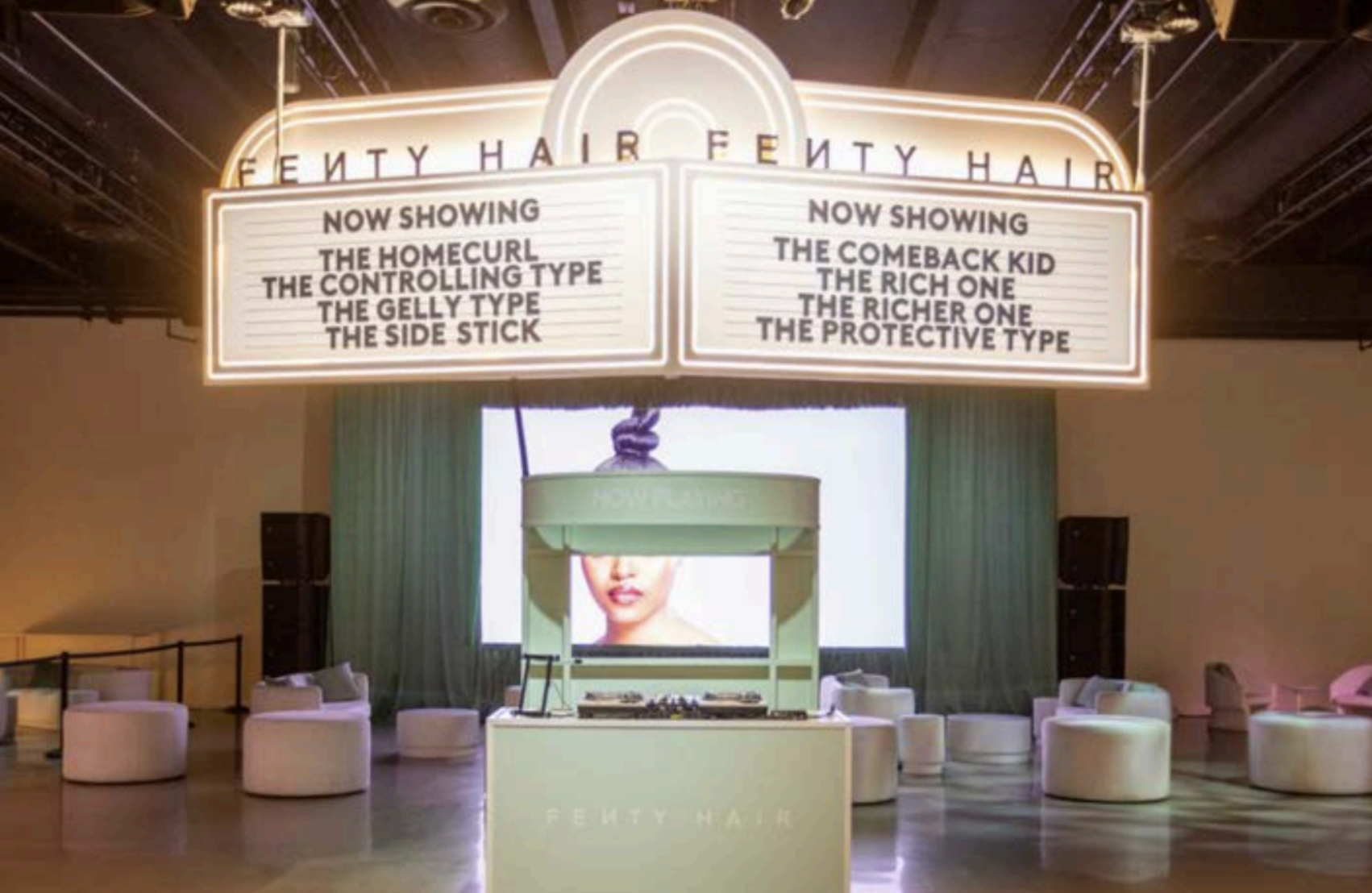 A large, illuminated signboard displays movie titles and showtimes in a theater lobby. The left side lists films available now, including 'The Homecurl,' 'The Controlling Type,' 'The Gelly Type,' and 'The Side Stick.' The right side lists upcoming sh