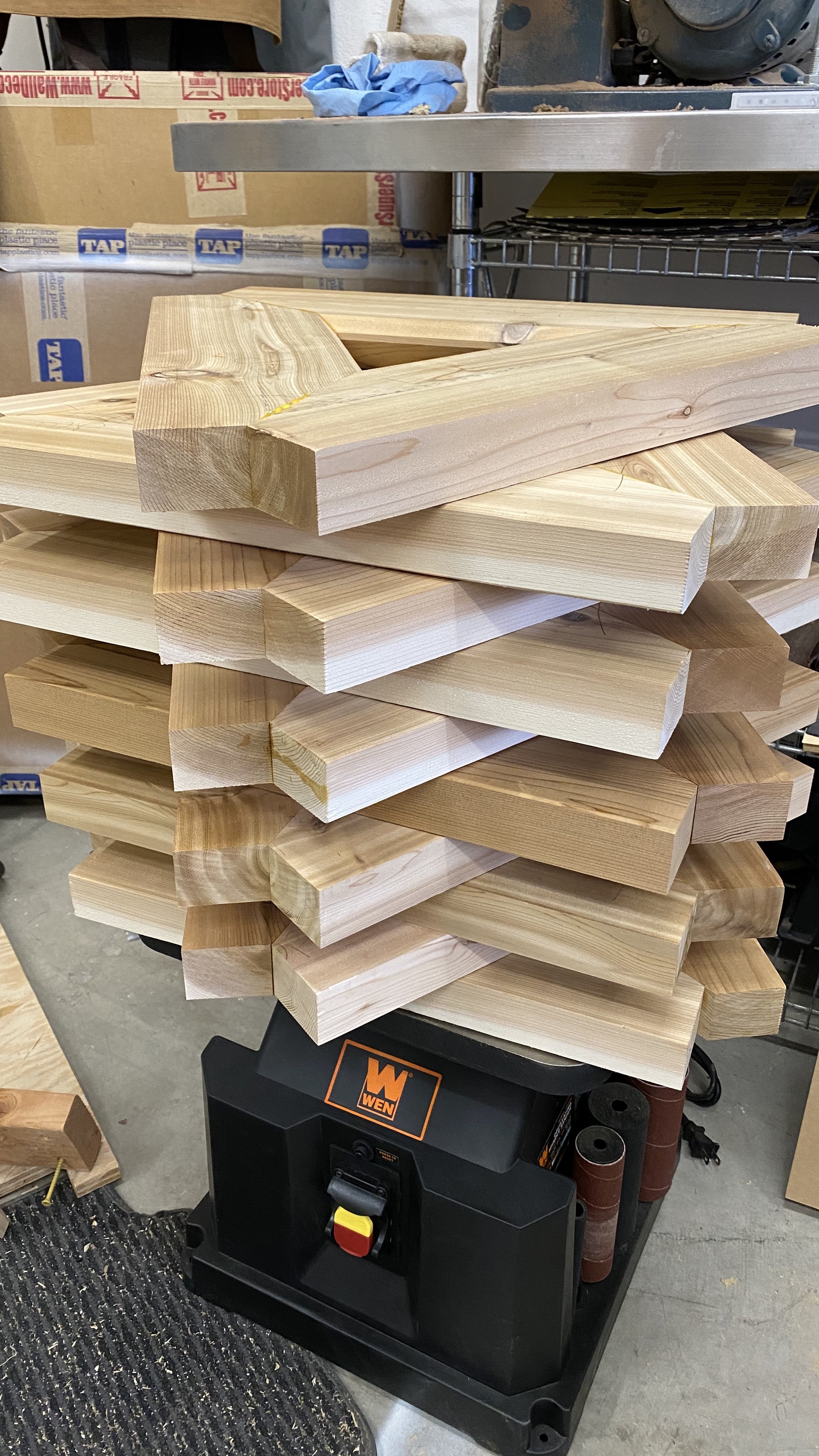 Stacked pieces of cut wood on a workbench with a power saw underneath, in a workshop.