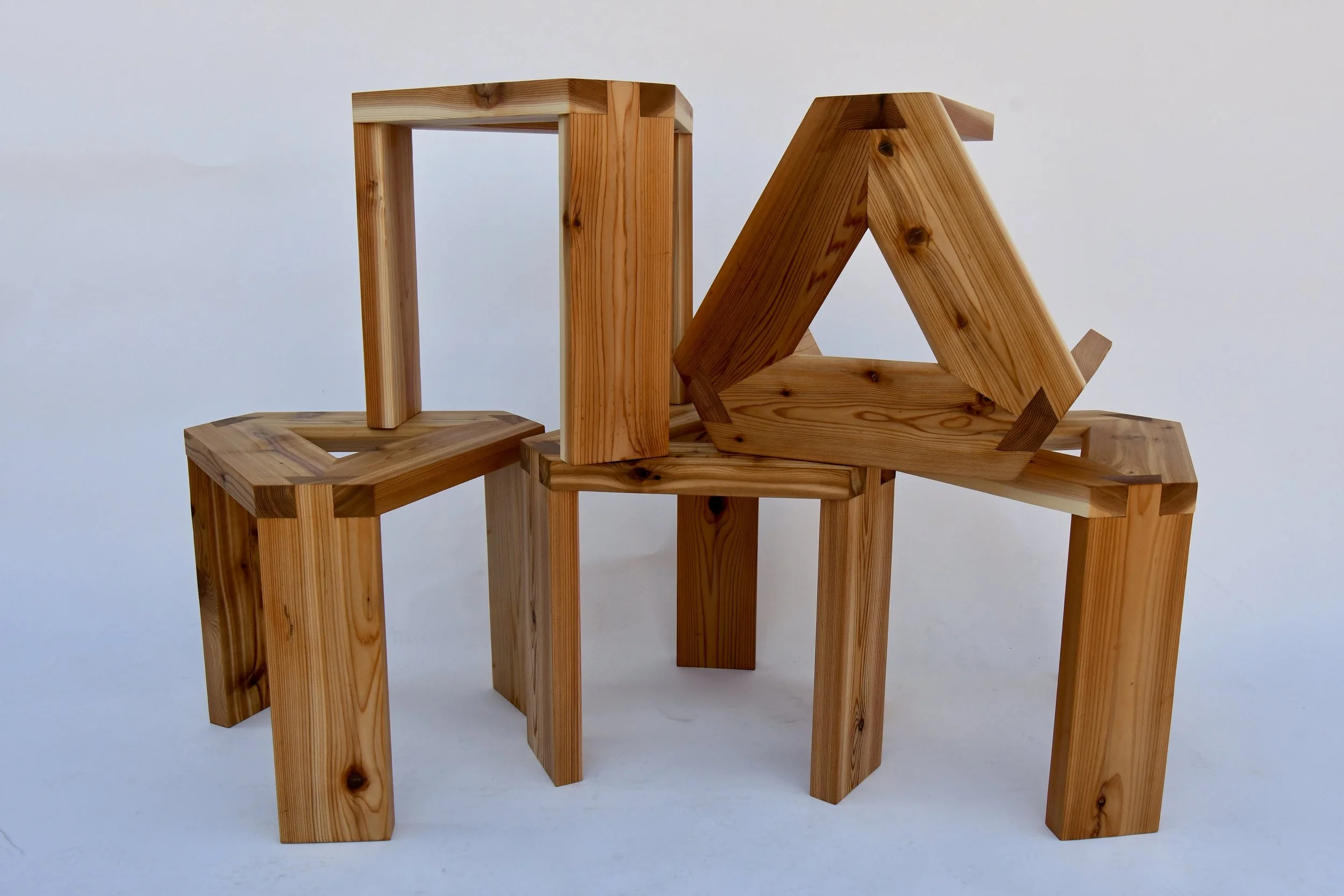 Multiple wooden stools arranged closely together against a plain background.