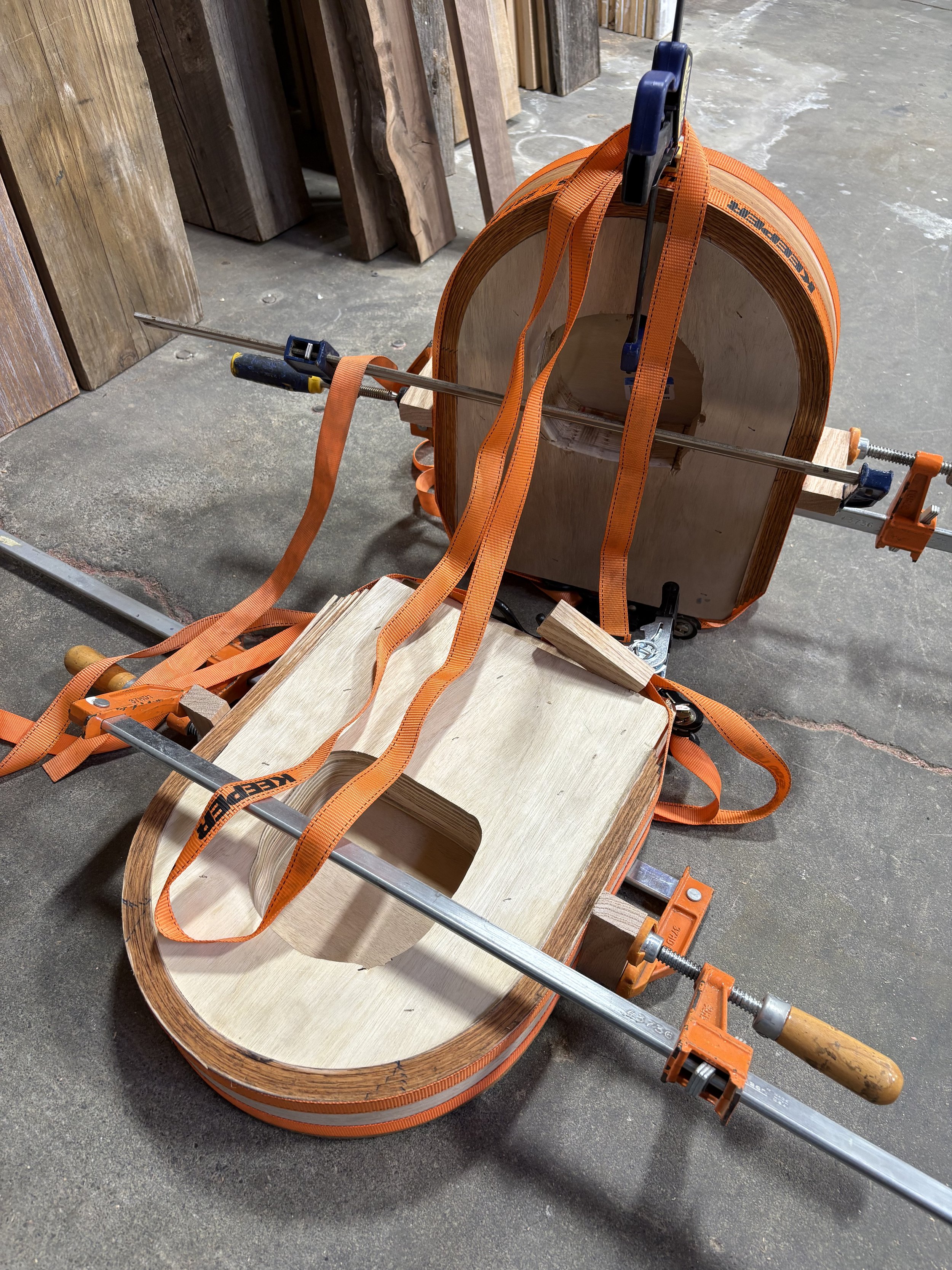 Wooden guitar body clamped on a workbench with orange straps in a woodworking shop.